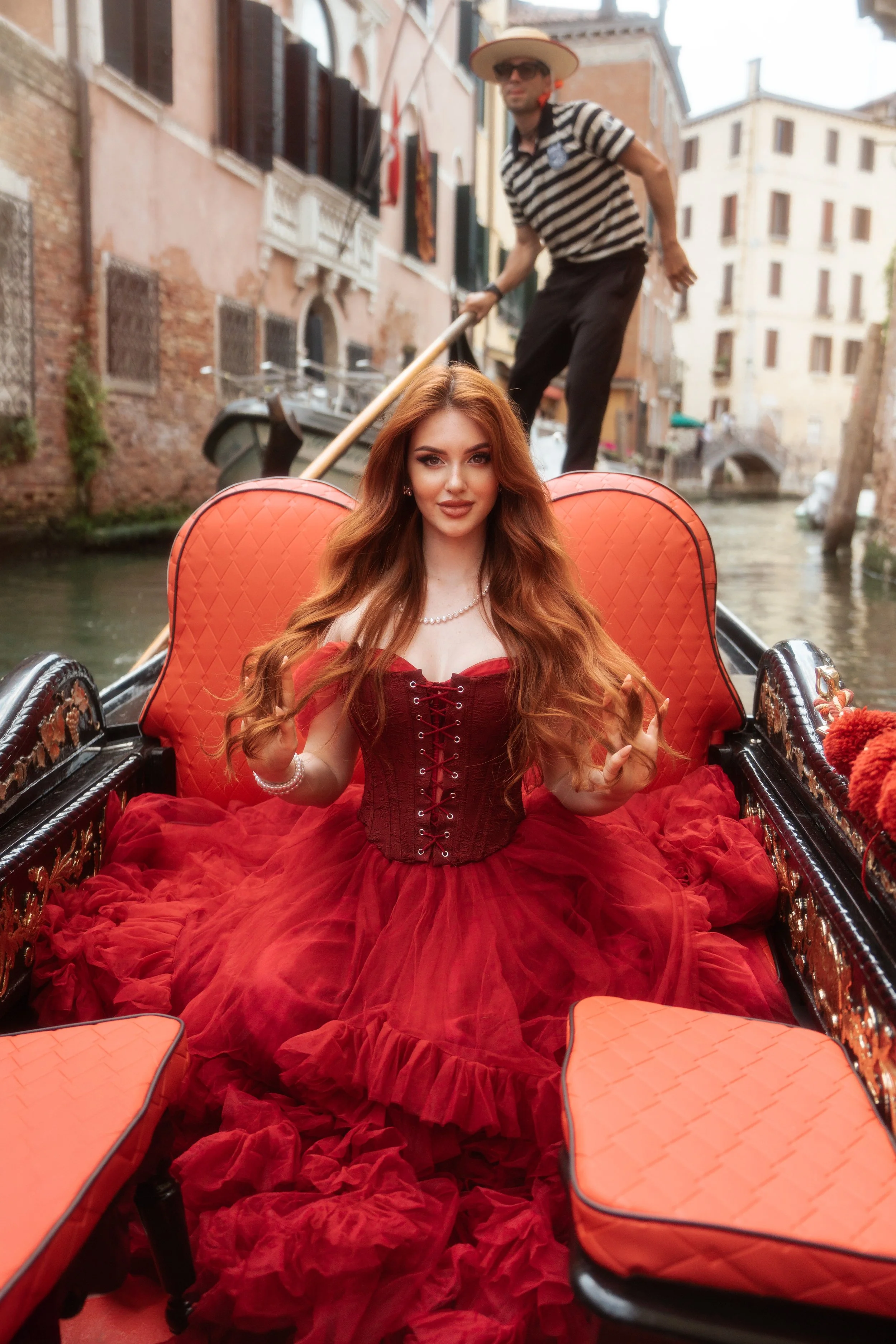 Modella dai capelli rossi in abito rosso durante uno shooting su una gondola a Venezia.