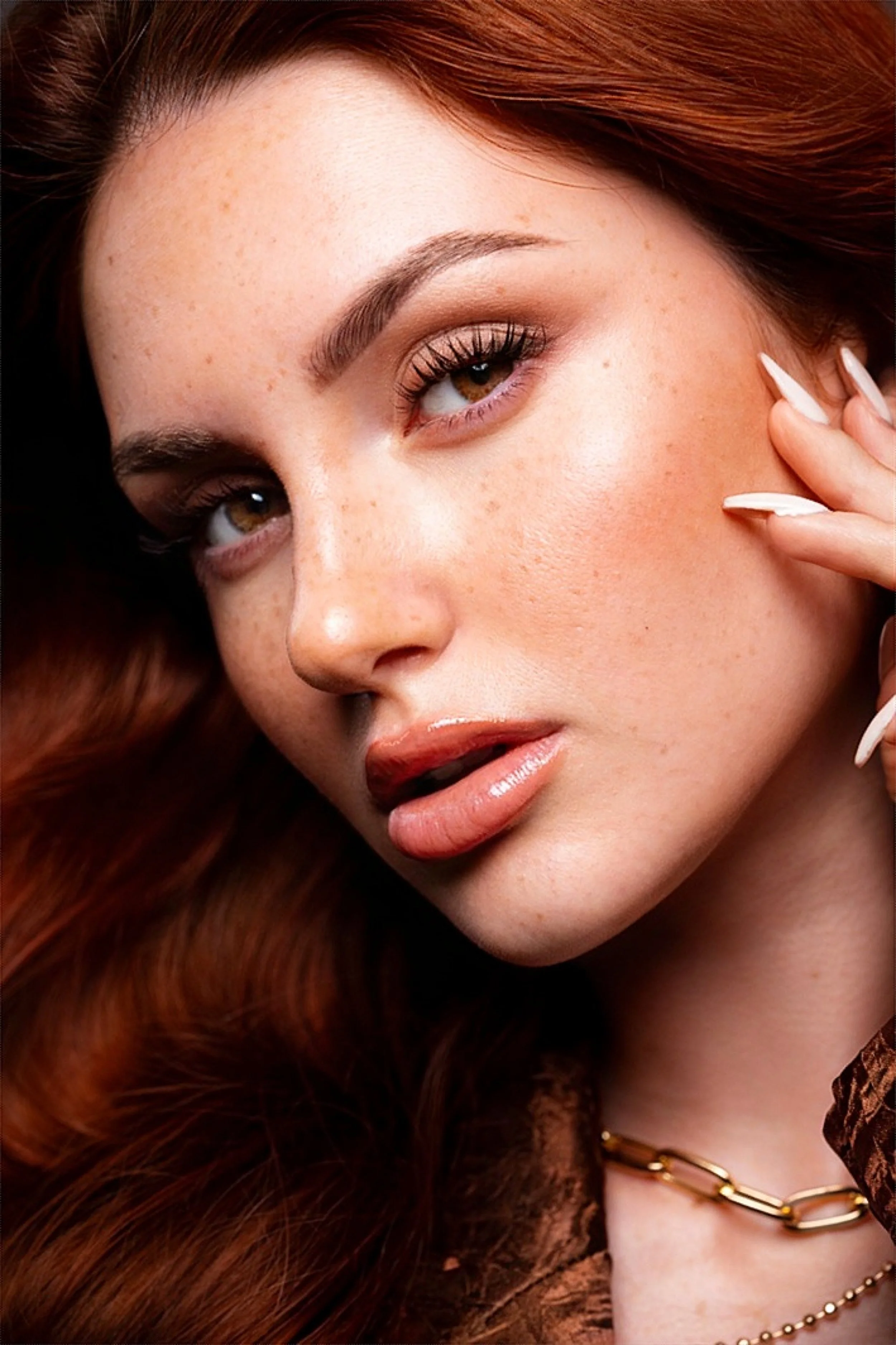 Primo piano beauty di Asia Zeggio, modella dai capelli rossi, con make-up luminoso e collana dorata.