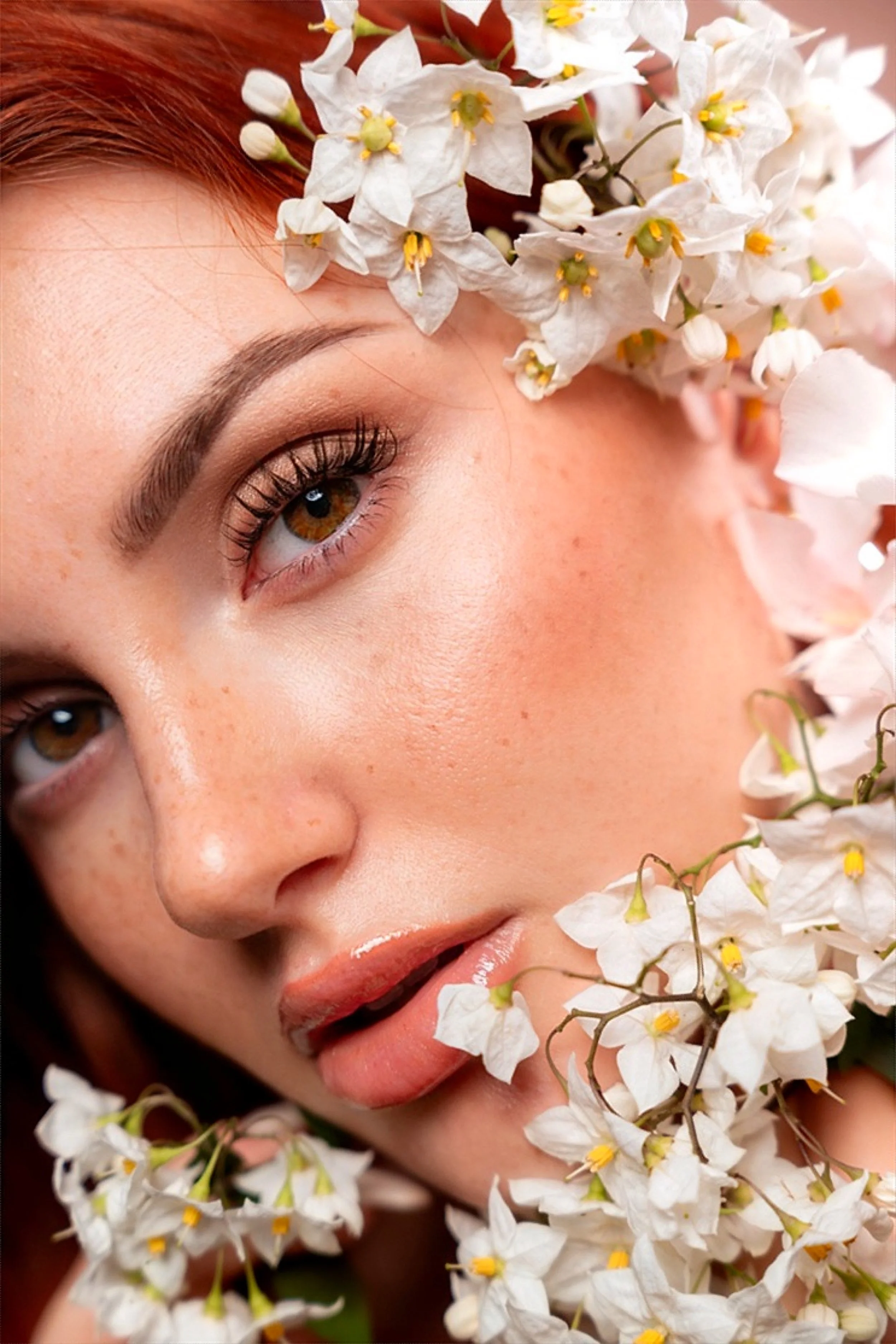 Volto di donna con capelli castani e occhi marroni, circondato da fiori bianchi.
