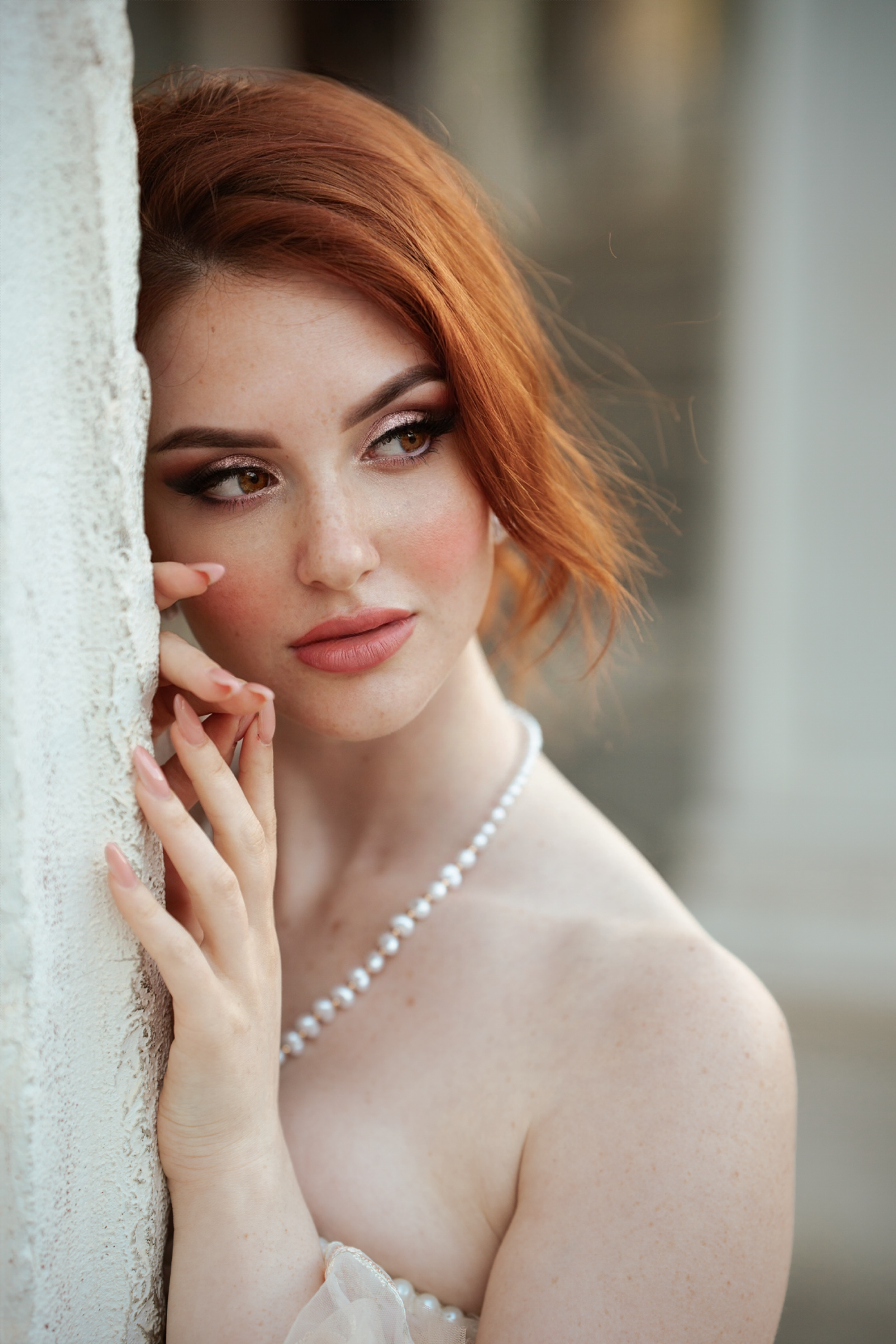 Ritratto beauty di modella dai capelli rossi con collana di perle e make-up intenso su sfondo chiaro.
