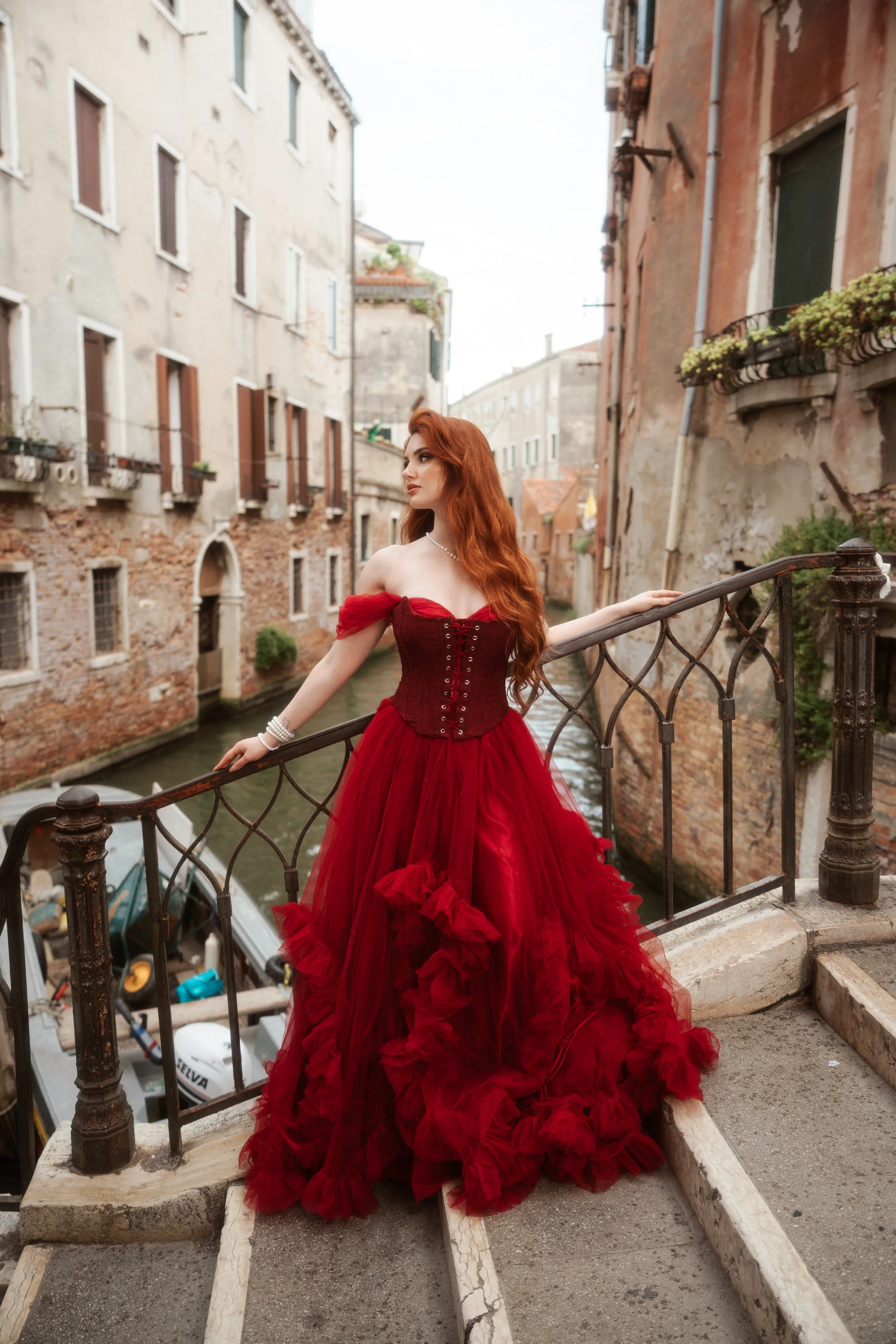 Modella dai capelli rossi in abito rosso durante uno shooting fashion tra le vie di Venezia.