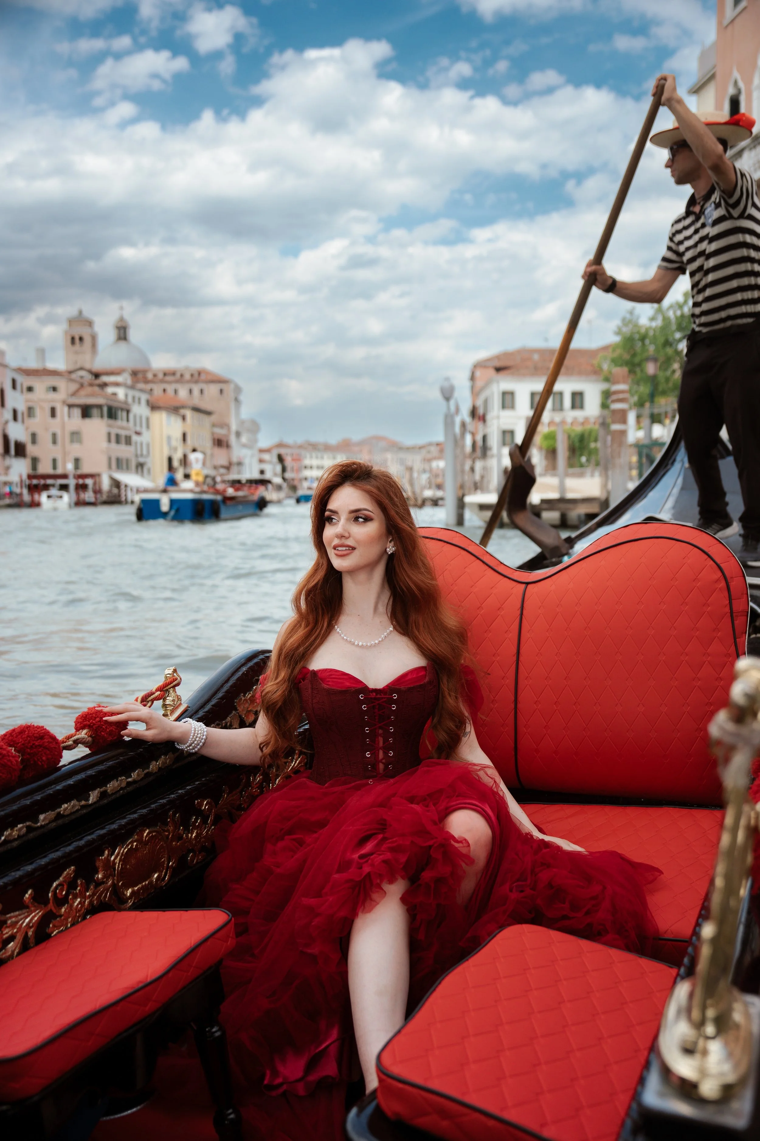 Shooting editoriale a Venezia con modella in abito rosso seduta su una gondola.
