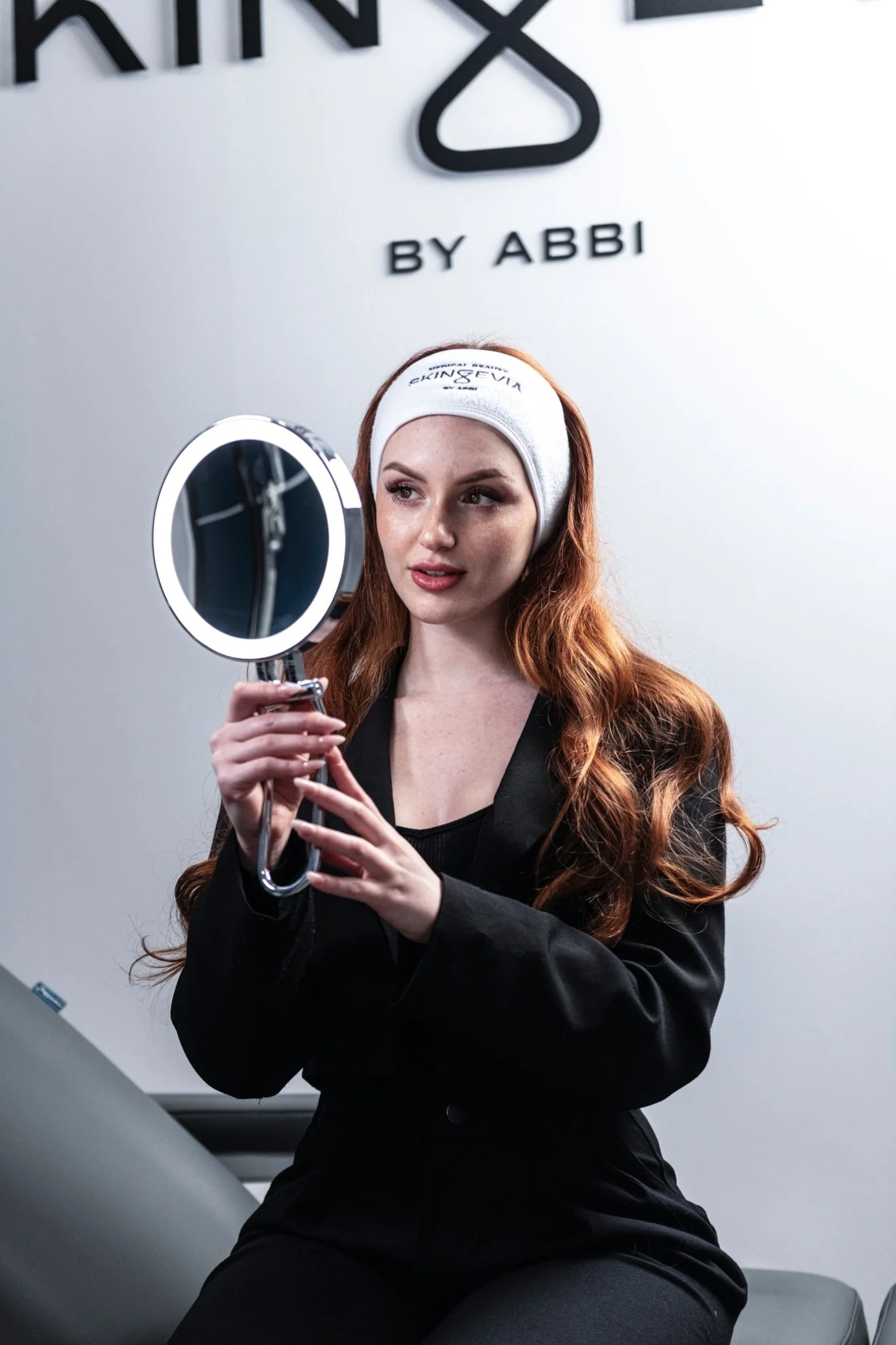 Asia Zeggio durante un contenuto beauty in salone, davanti allo specchio, con fascia bianca tra i capelli.
