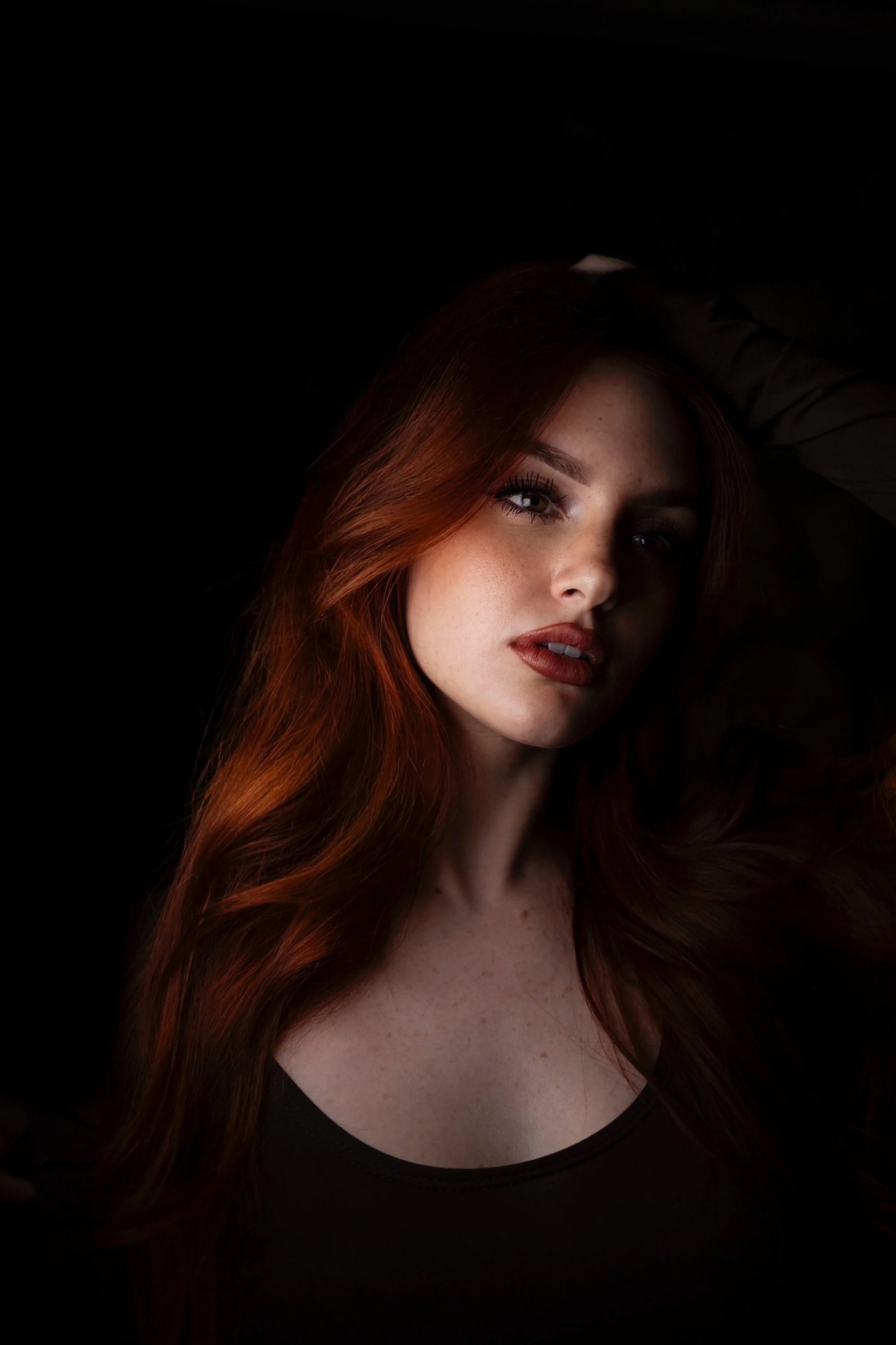 Ragazza con lunghi capelli rossi, che guarda l'obiettivo, con sfondo nero.