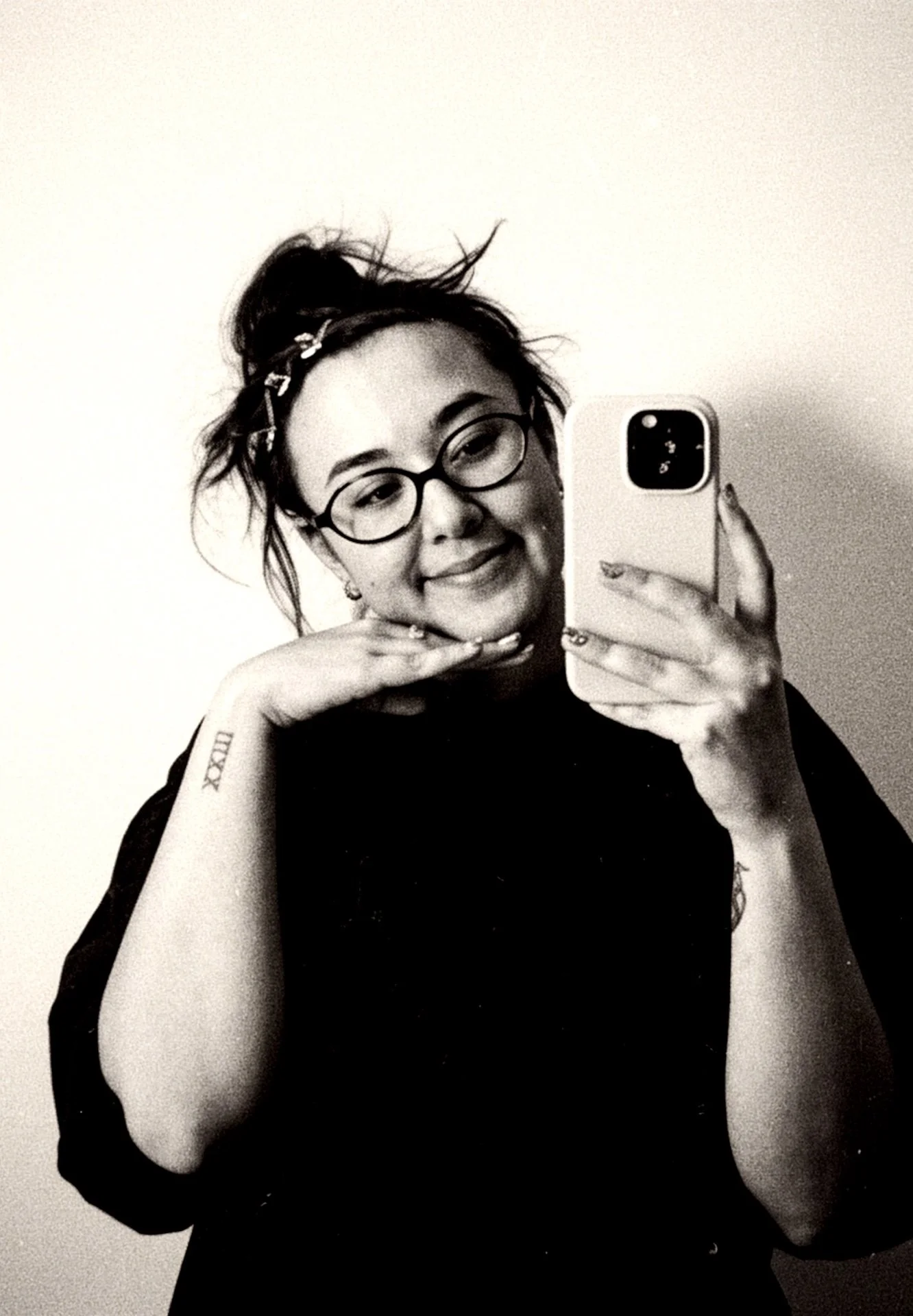 A woman with glasses taking a selfie in a mirror. She has her hair tied up with a headband and is smiling.