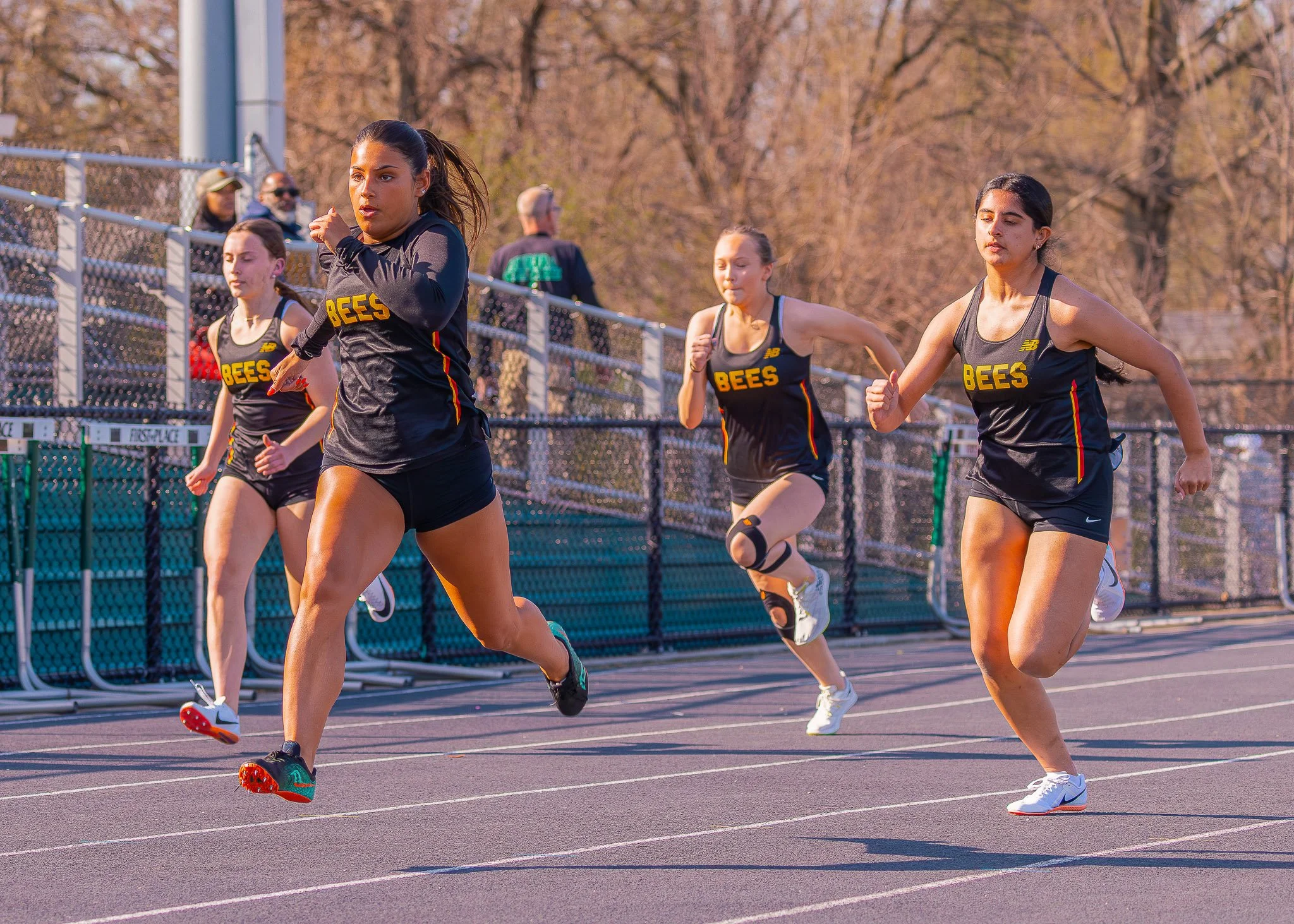 A group of young women running on a track during a race, wearing black and yellow 