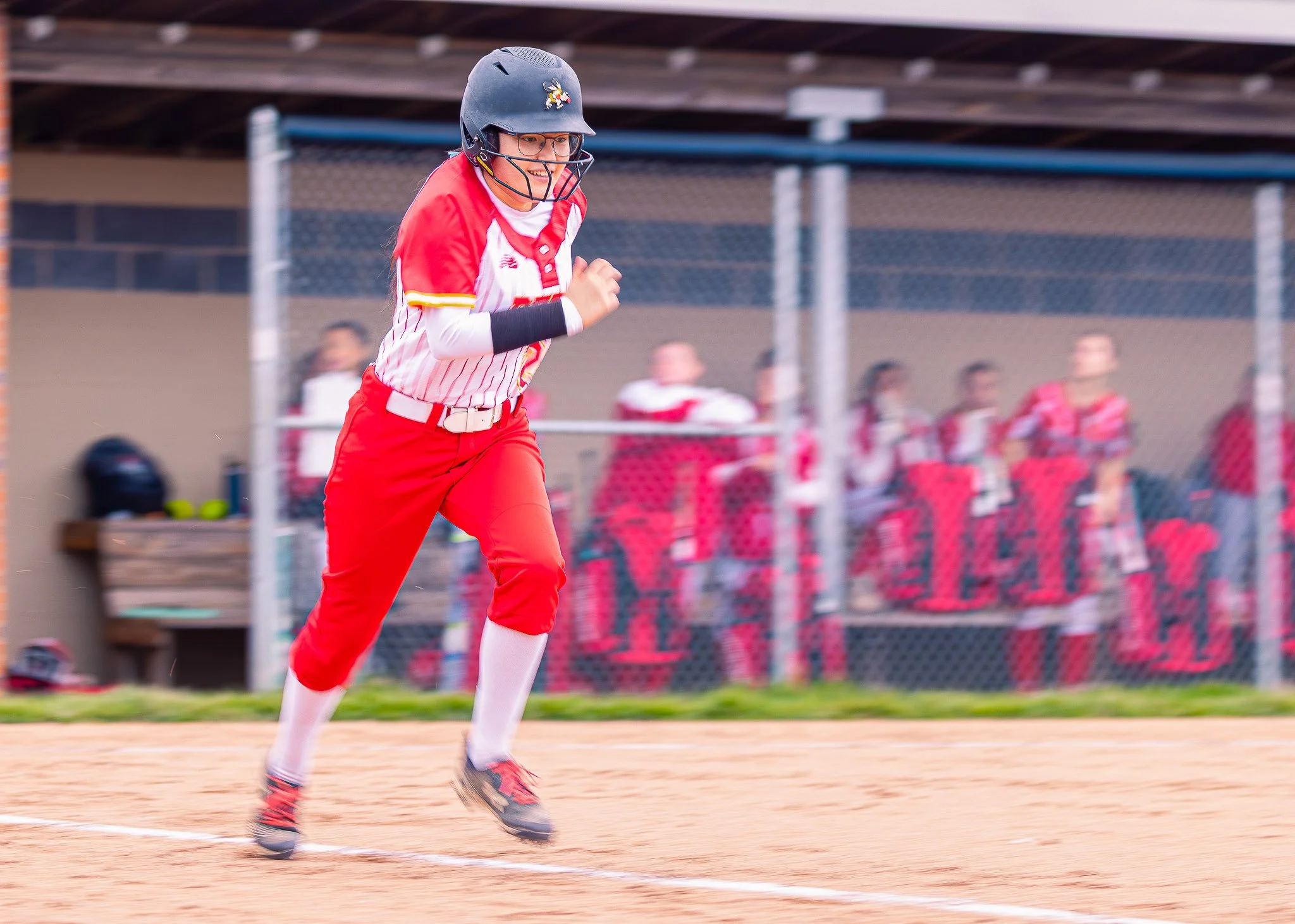 A woman wearing a black batting helmet, glasses, and a red-and-white baseball uniform running on a baseball field.