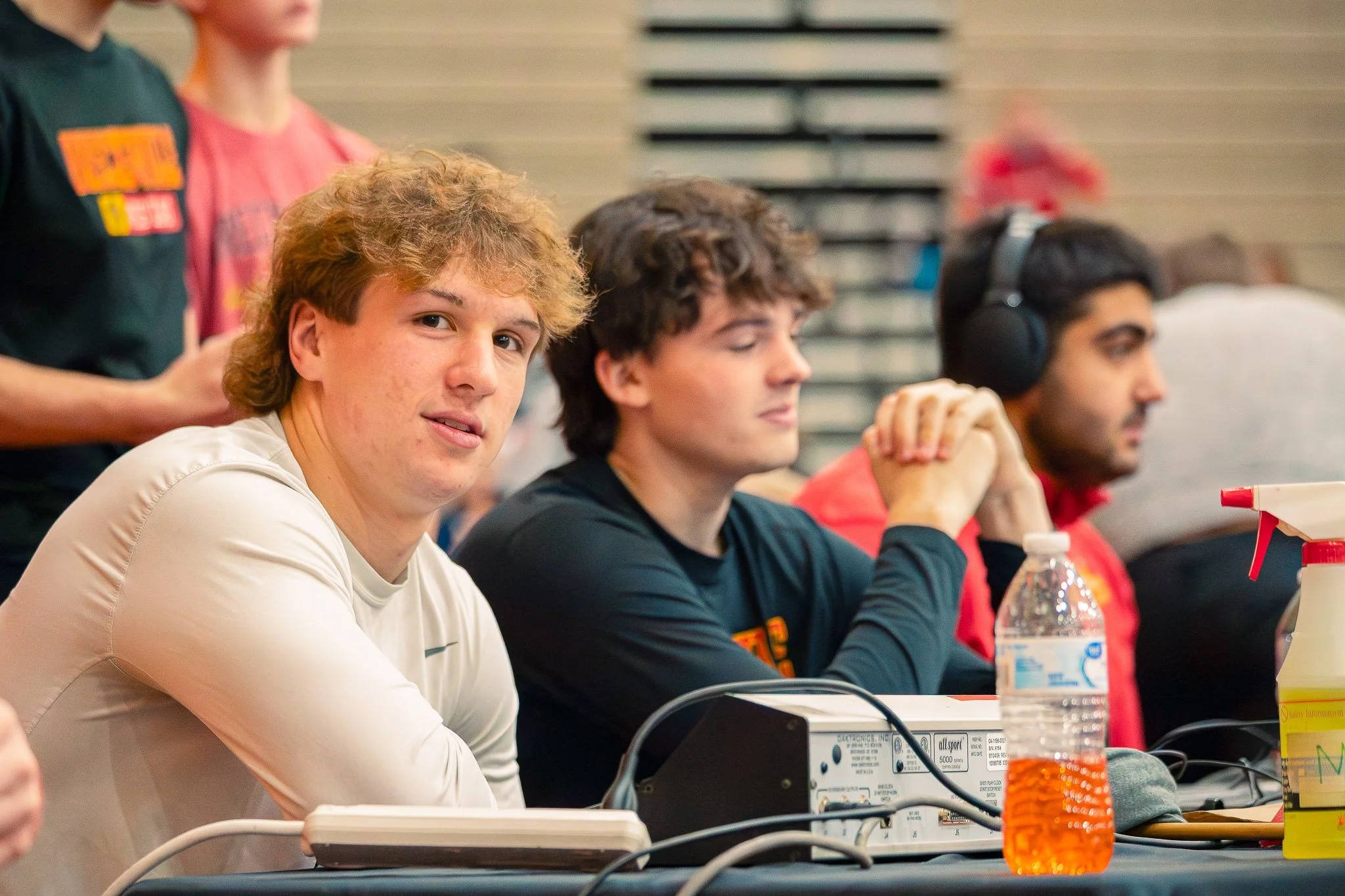 Young men sitting at a commentator's booth during a wrestling match.
