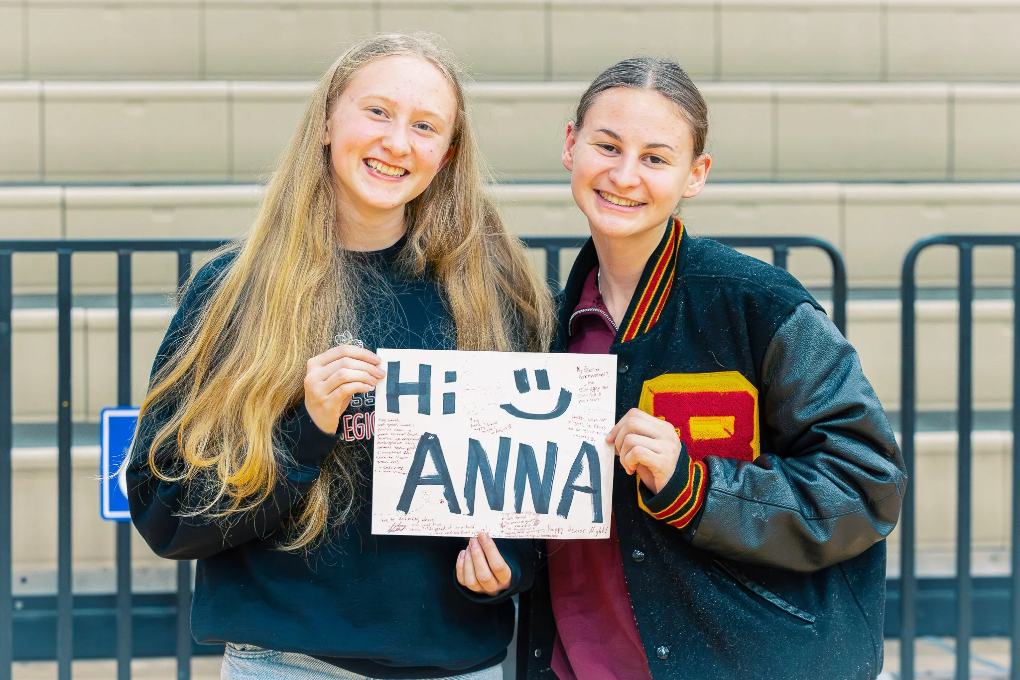 Two young women smiling and holding a sign that says 'Hi ANNA' with handwritten messages.