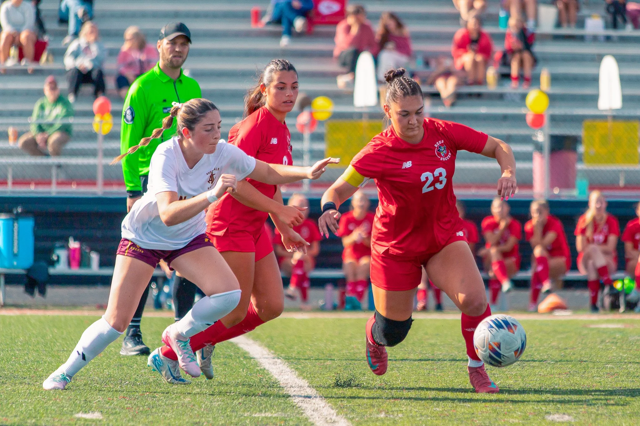 Girls playing soccer on a field while an official watches in the background.