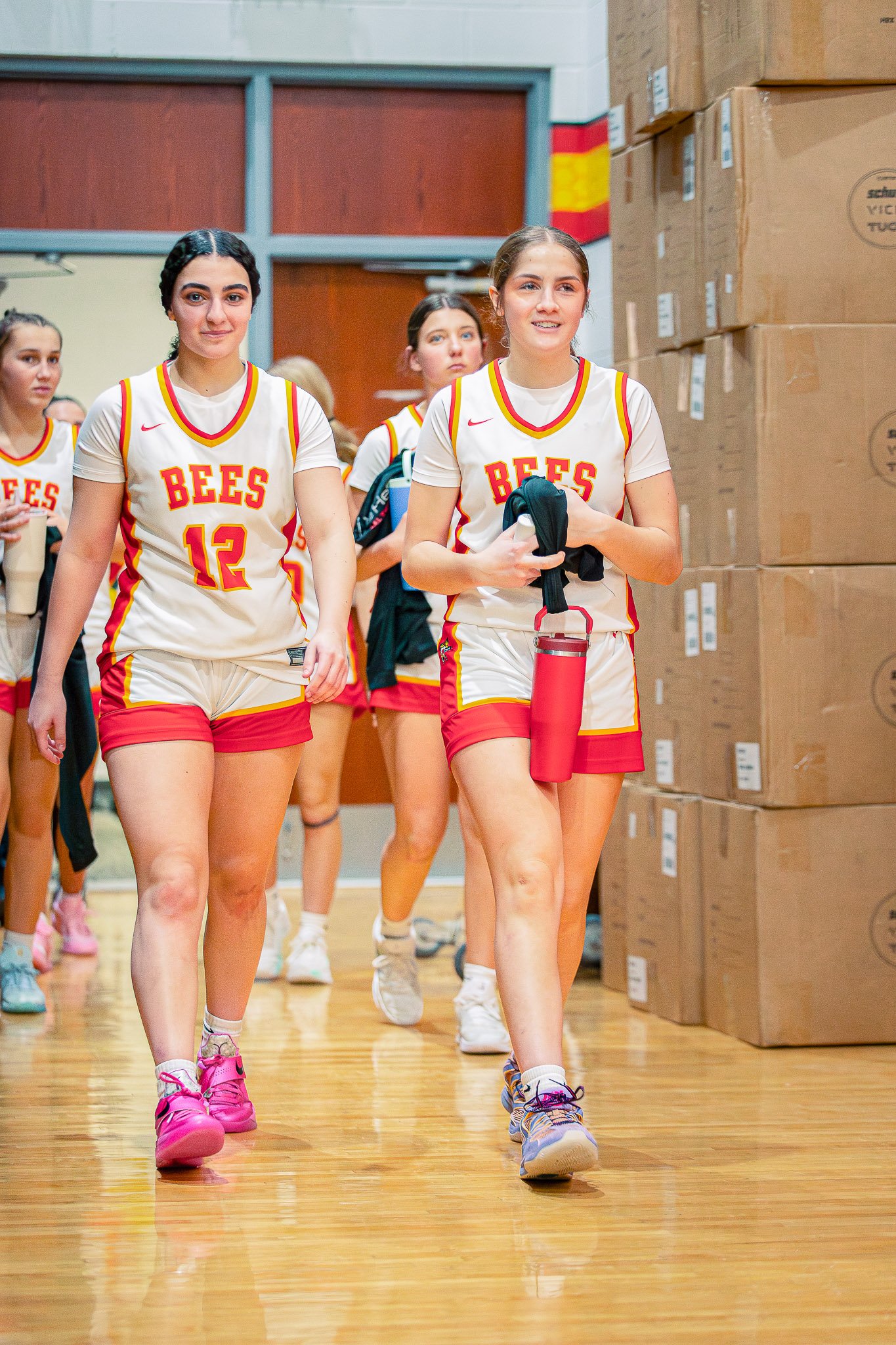 Group of young female basketball players walking in a gymnasium, wearing basketball jerseys