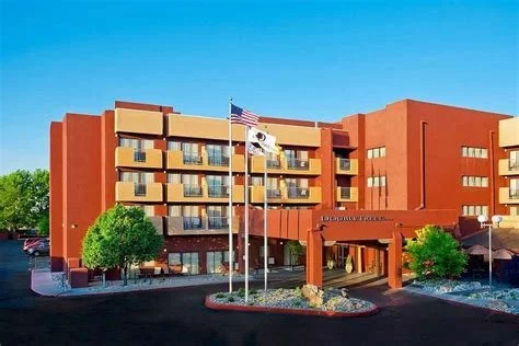 Exterior view of a multi-story hotel building with flagpoles and landscaped entrance.