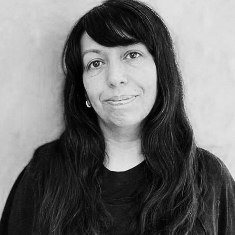 Black and white portrait of a professional with long dark hair, wearing a dark top, looking at the camera with a slight smile