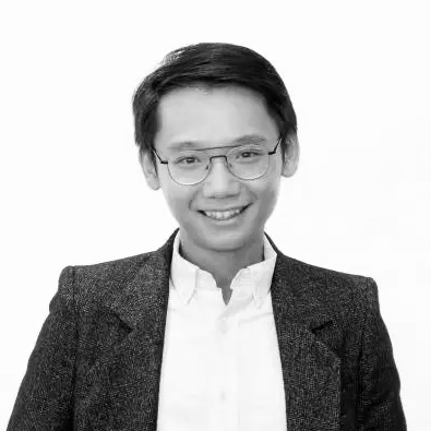 Black and white portrait of a smiling professional with short hair and glasses, wearing a blazer and white shirt.