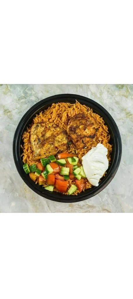 A black bowl of rice topped with fried chicken, chopped cucumbers and tomatoes, a dollop of sour cream or yogurt, and a slice of baked fish.