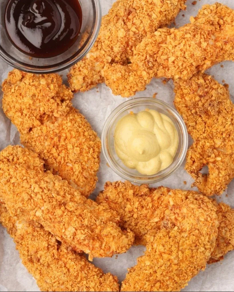 Six pieces of breaded and fried chicken tenders served with two dipping sauces, one dark and one light, on a sheet of paper