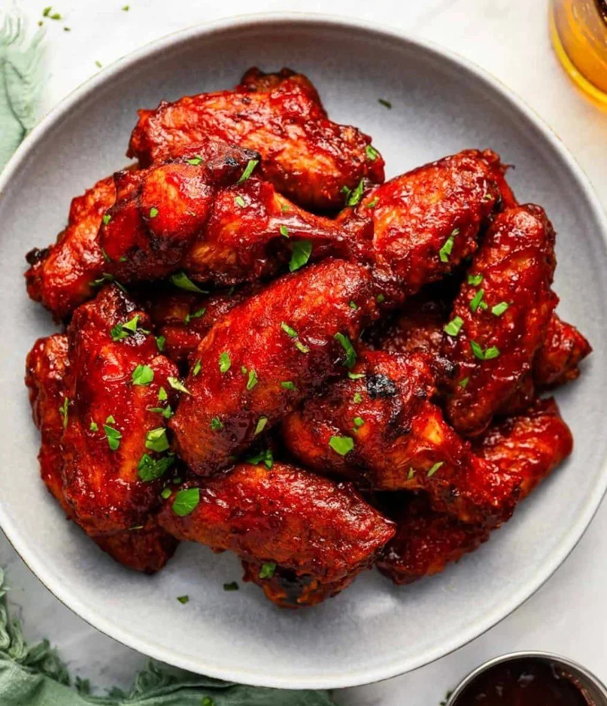 A bowl of spicy buffalo chicken wings garnished with chopped green herbs, served with dipping sauce on the side.