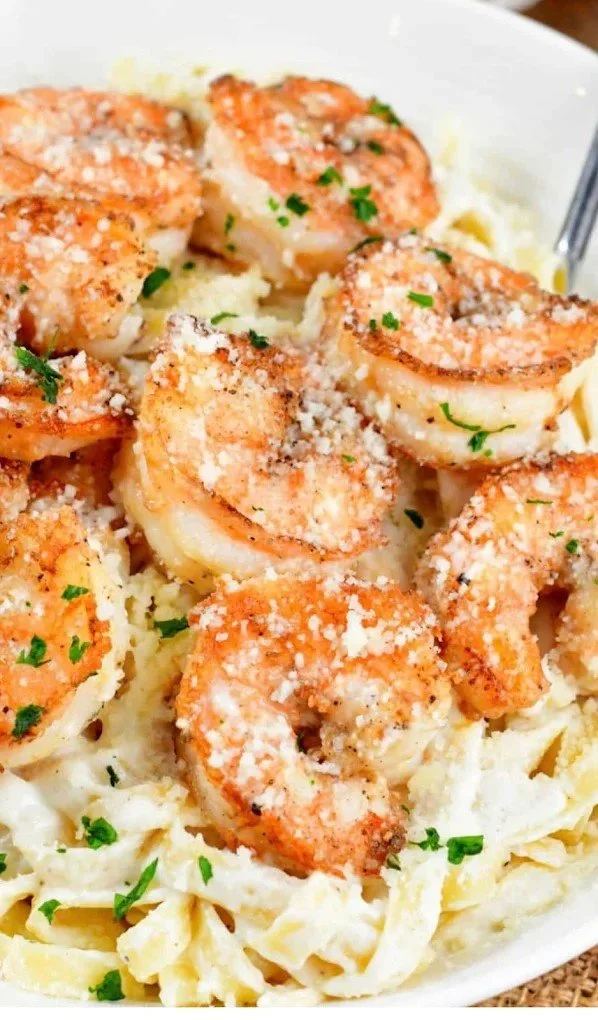 Shrimp scampi with cooked shrimp, grated cheese, chopped parsley, over linguine pasta in a white bowl.
