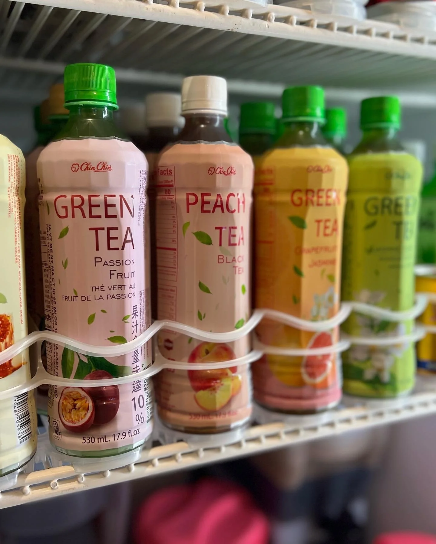 Various bottles of flavored teas on a store shelf, including green tea and peach tea, with some bottles showing fruit illustrations and labels in multiple languages.