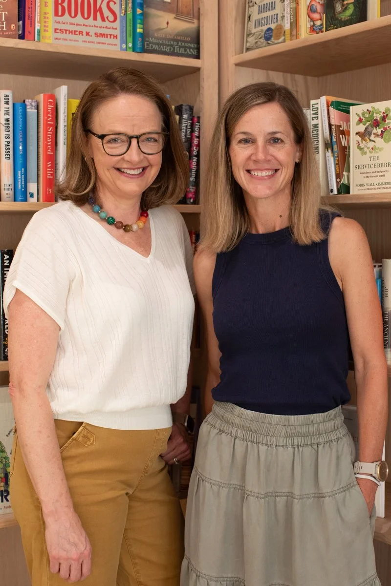 Two women standing in front of bookshelf filled with books, smiling at the camera.