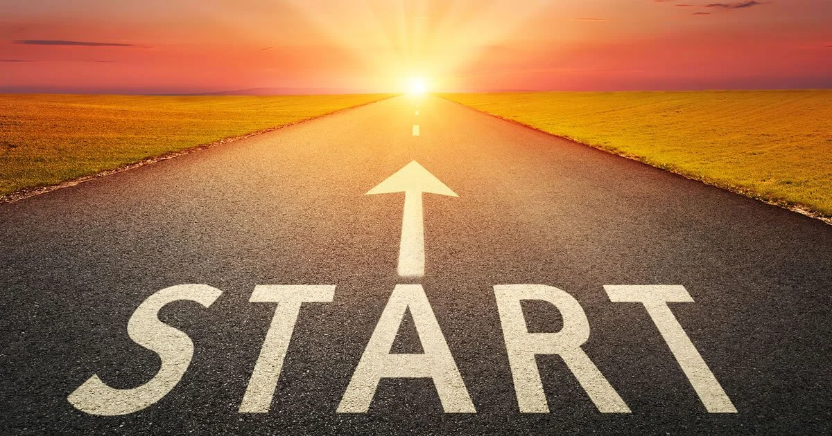 A road with a large white start line and an upward arrow, leading toward a bright sunrise on the horizon, flanked by grassy fields.