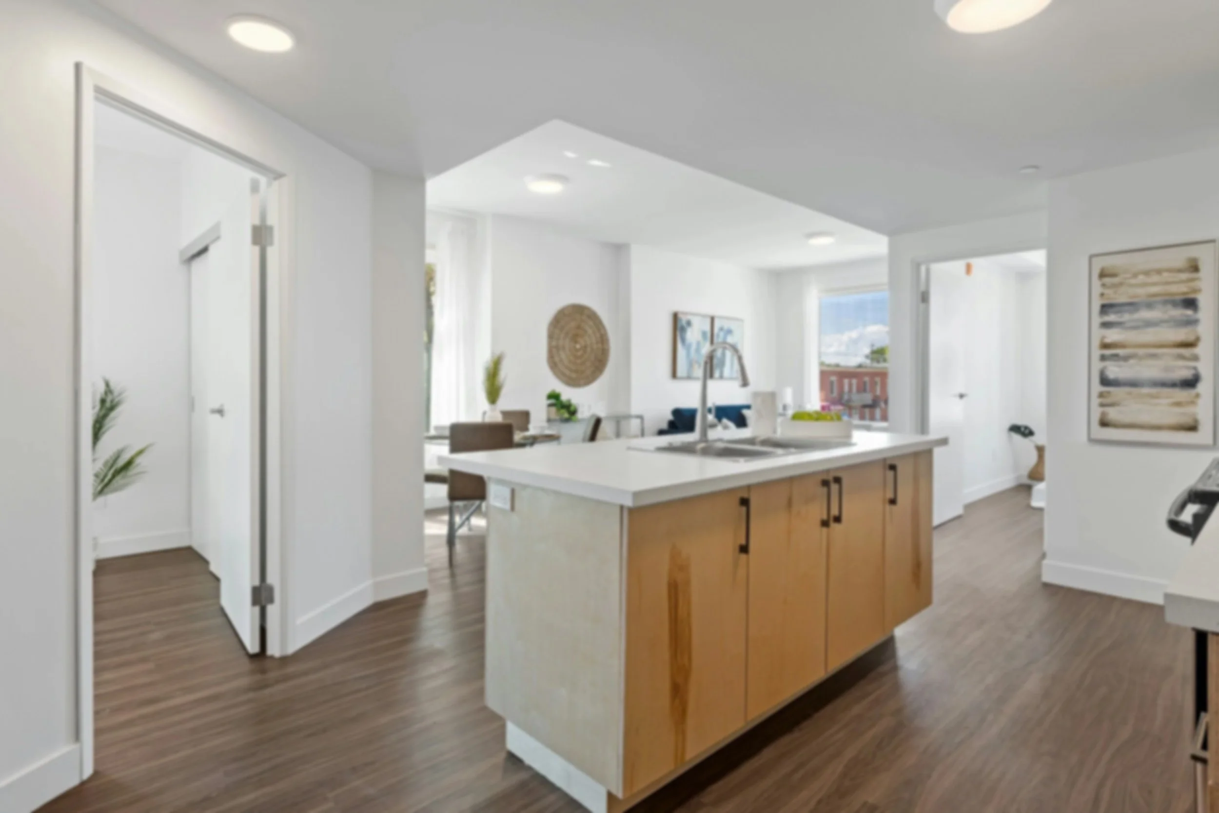 Modern kitchen with an island, sink, and wooden cabinets, bright with large windows and open layout.