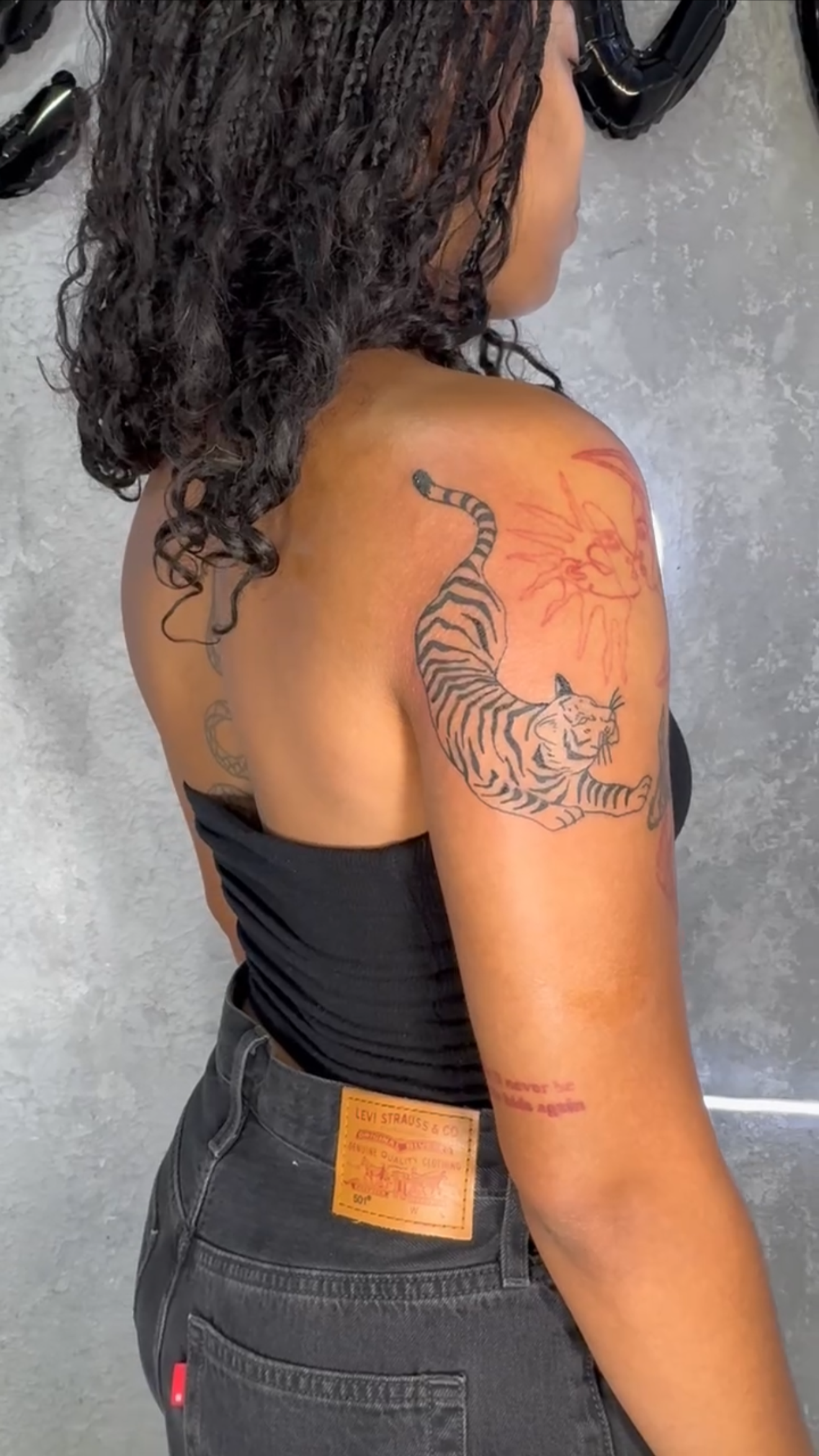 A woman with curly hair showing a tiger tattoo on her shoulder and upper arm.