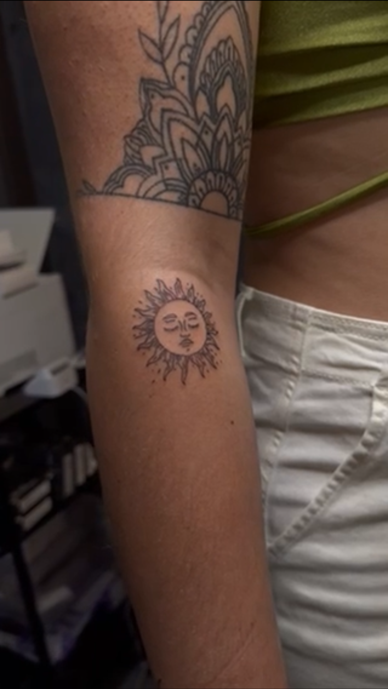 Tattoo of a sun with a human face on a person's upper arm, and a decorative mandala-like design on the shoulder.