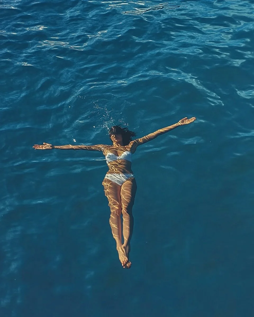A woman in a bikini floating on her back in a body of water, with her arms extended to the sides.