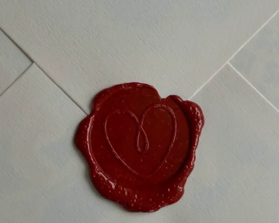 A red wax seal with a heart shape pressed into it, attached to a tiled surface.