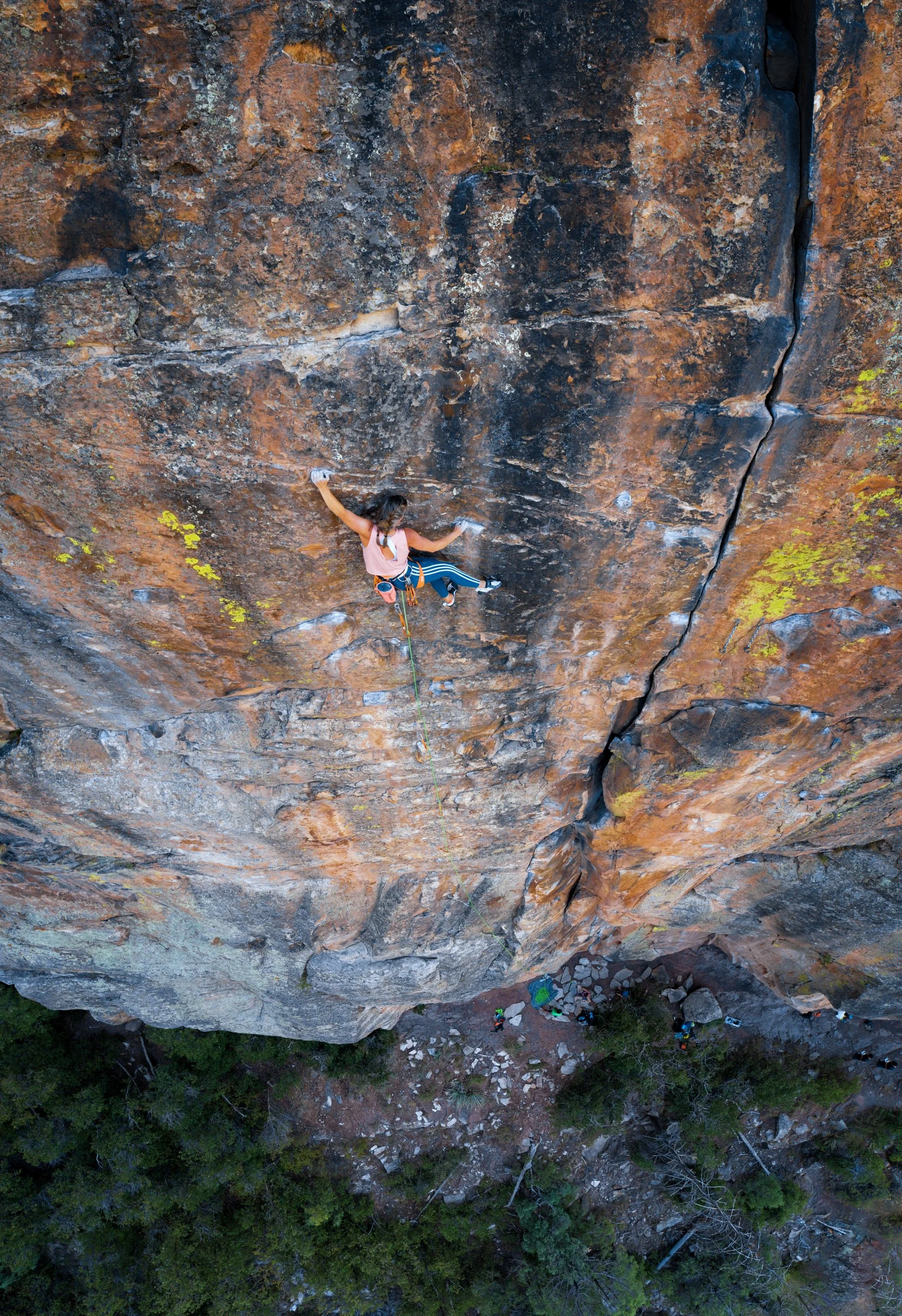A person rock climbing on a steep, orange-brown granite cliff, with a green forest at the bottom.