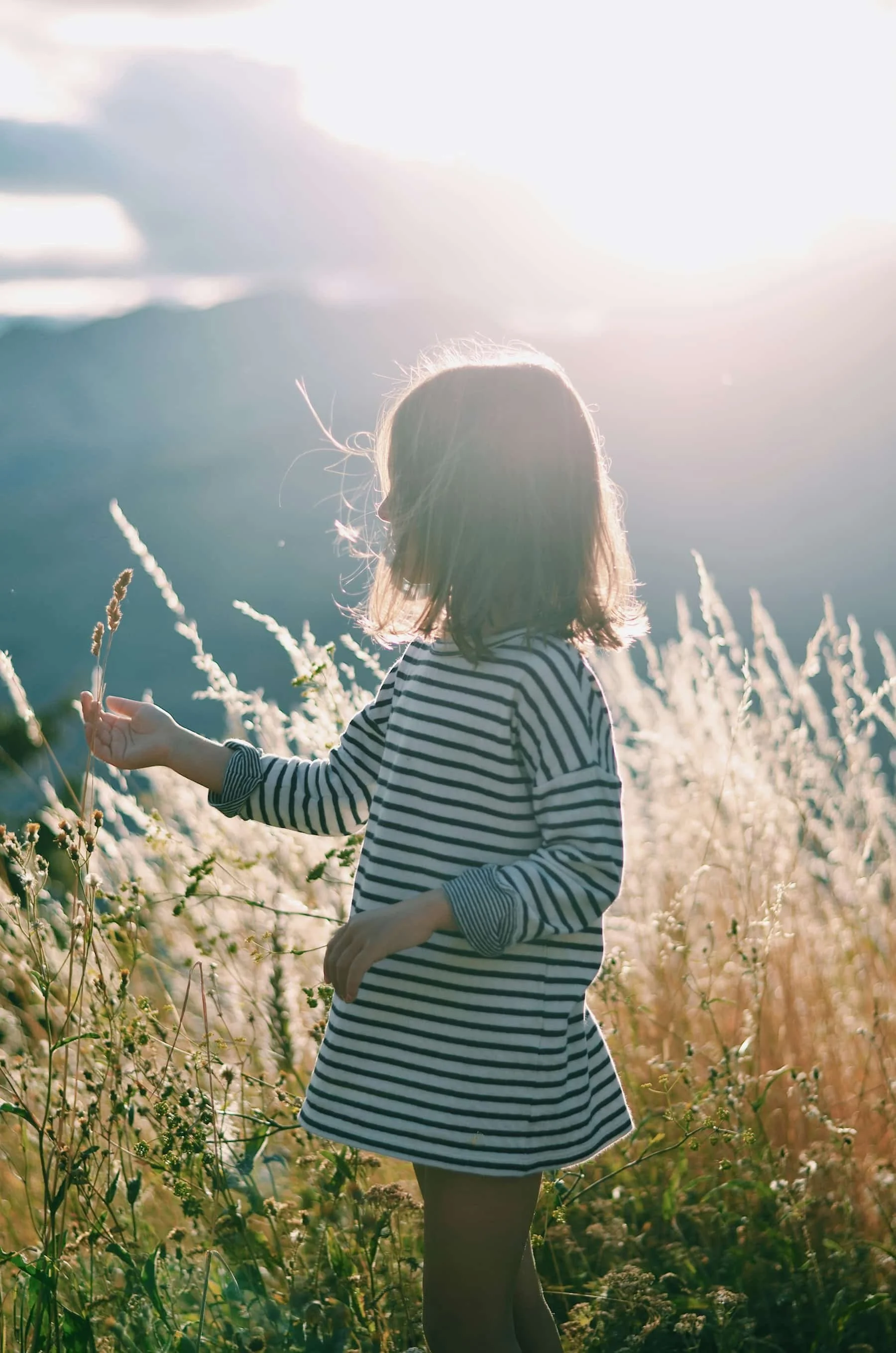 Girl walking through tall grass in warm sunlight, representing confidence and exploration.