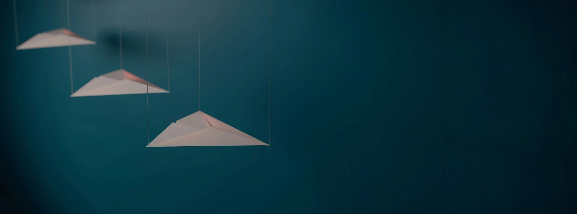 3 paper airplanes hanging by string and pointing in the same direction, against a dark blue background