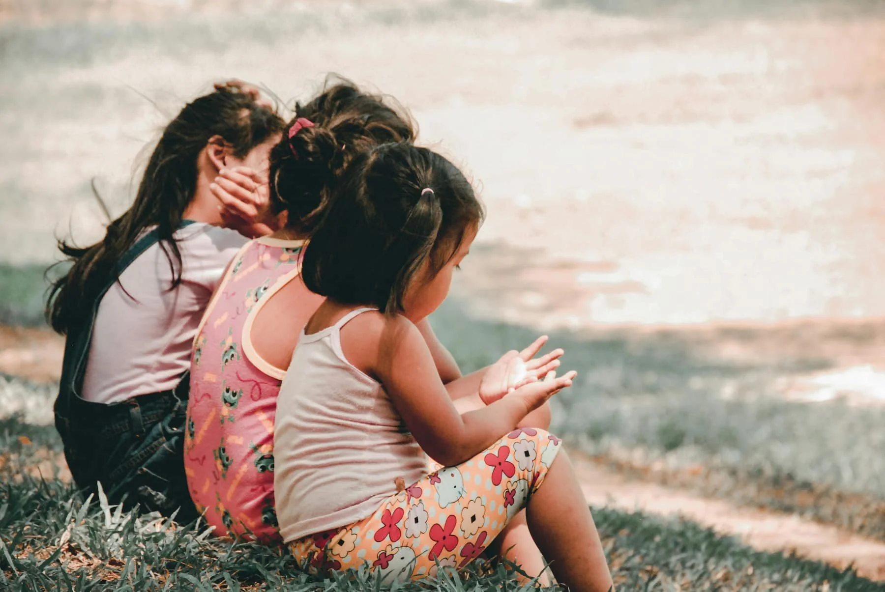Three young children sitting together on the grass, representing friendship and childhood connection.