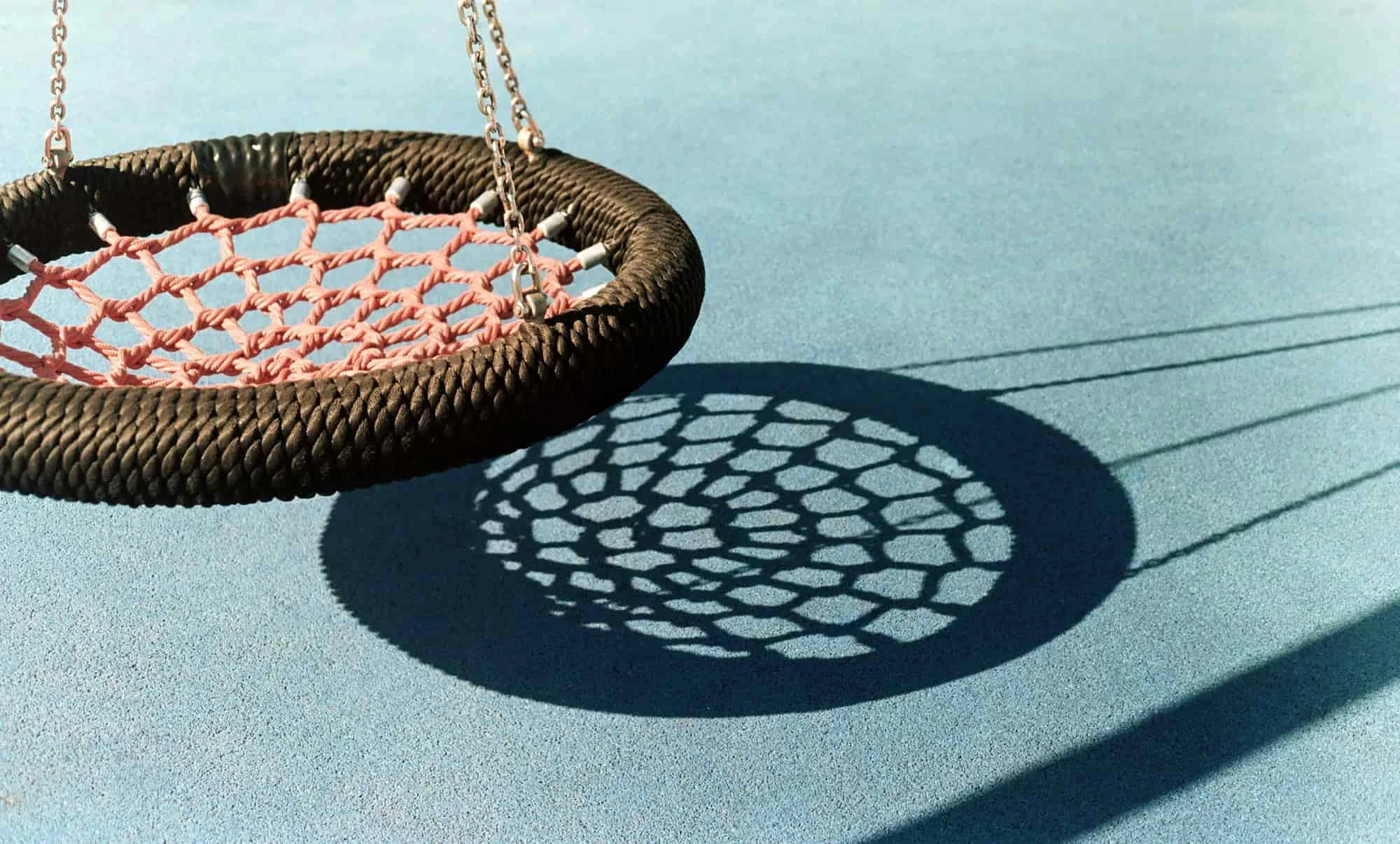 A large round net swing casting a shadow on a light blue court surface.