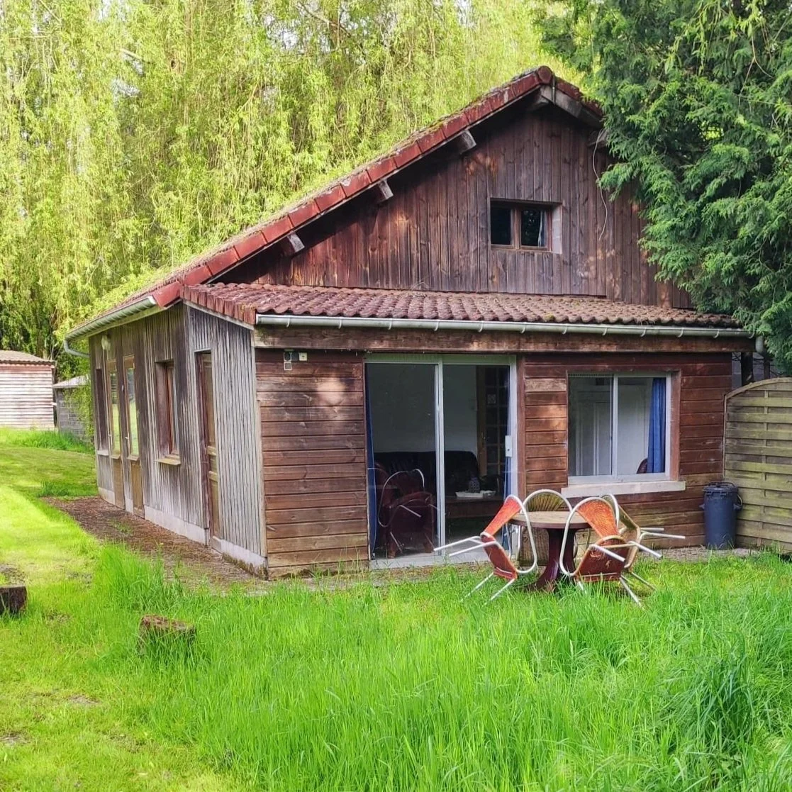 Een houten tuinhuis met een rode dak, omgeven door groen gras en bomen.