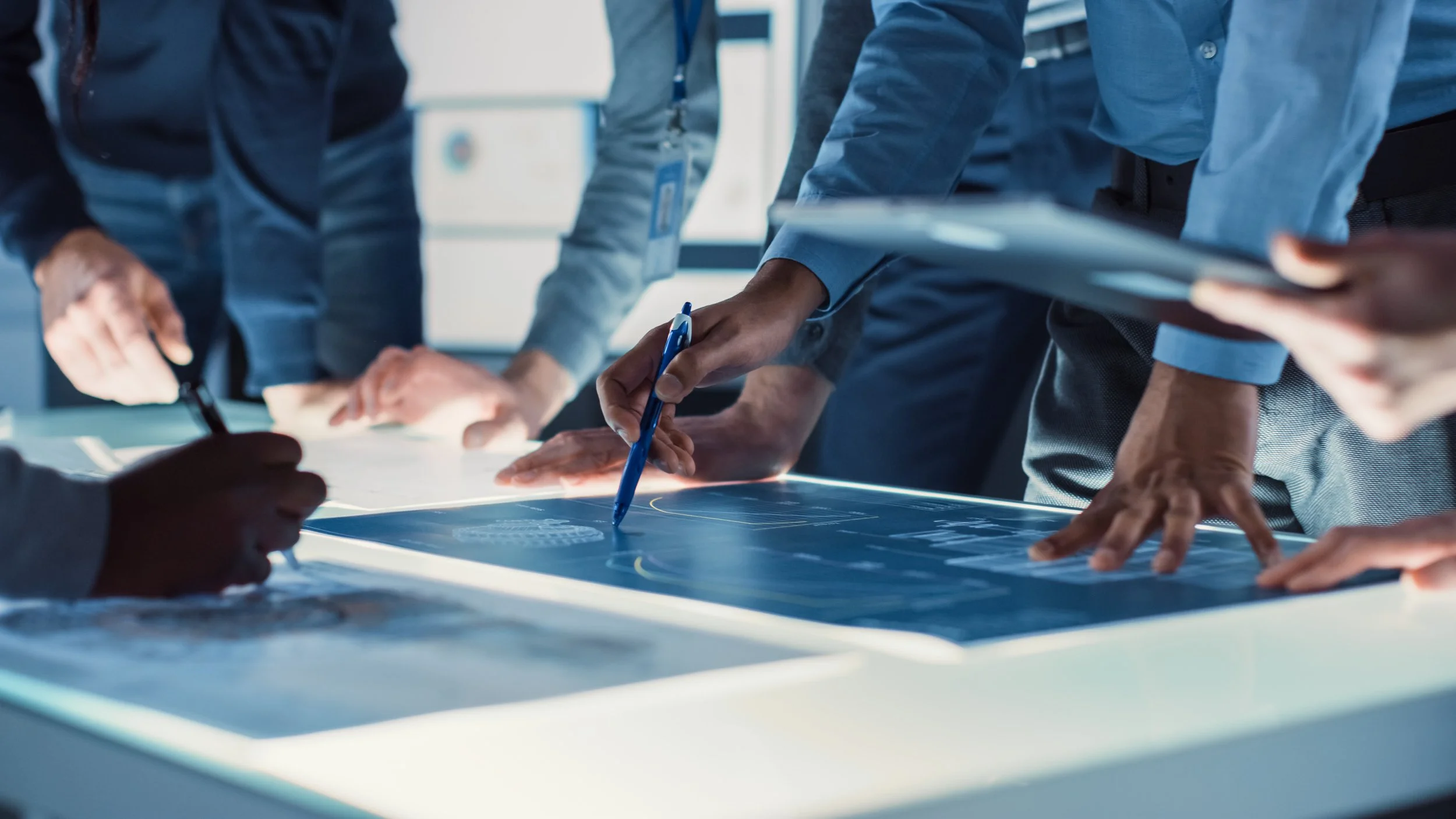 Group of people in business attire working on a large digital touchscreen table, analyzing data and discussing.