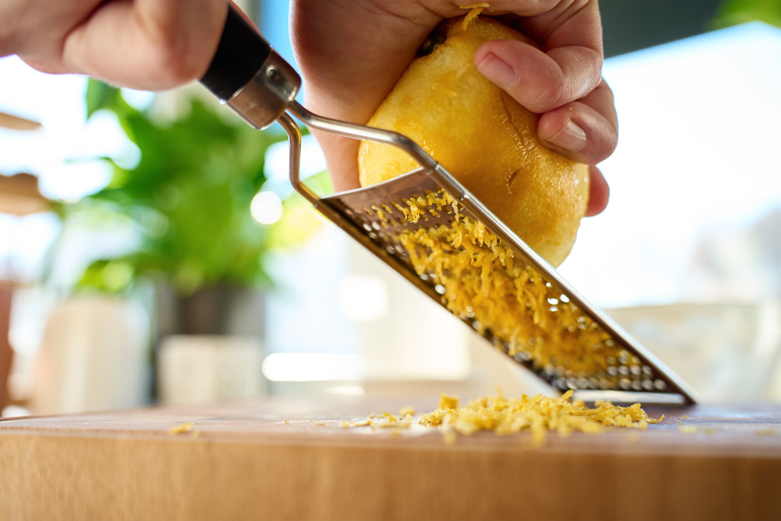 Person grating lemon zest over a wooden surface.