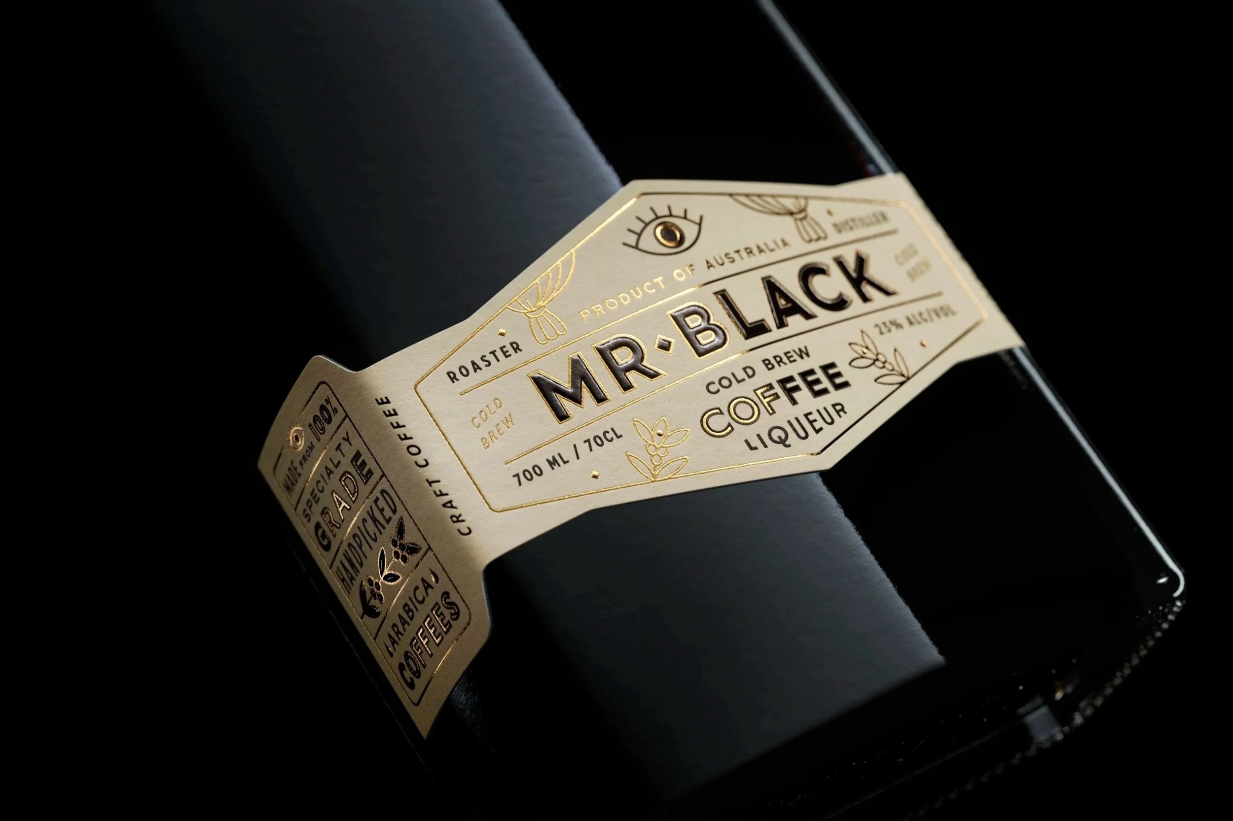 Close-up of a gold label on a dark bottle of Mr. Black coffee liqueur, with small text indicating it's a product of Australia, 25% alcohol, and that it contains cold brew coffee.