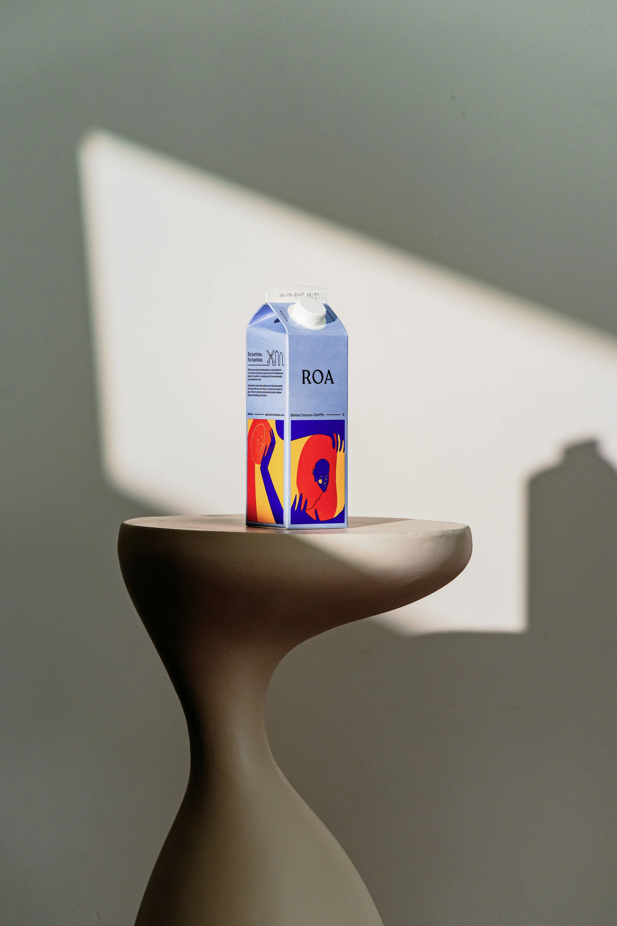 A carton of ROA coconut oat milk on a pedestal, with a shadow cast on the wall behind.
