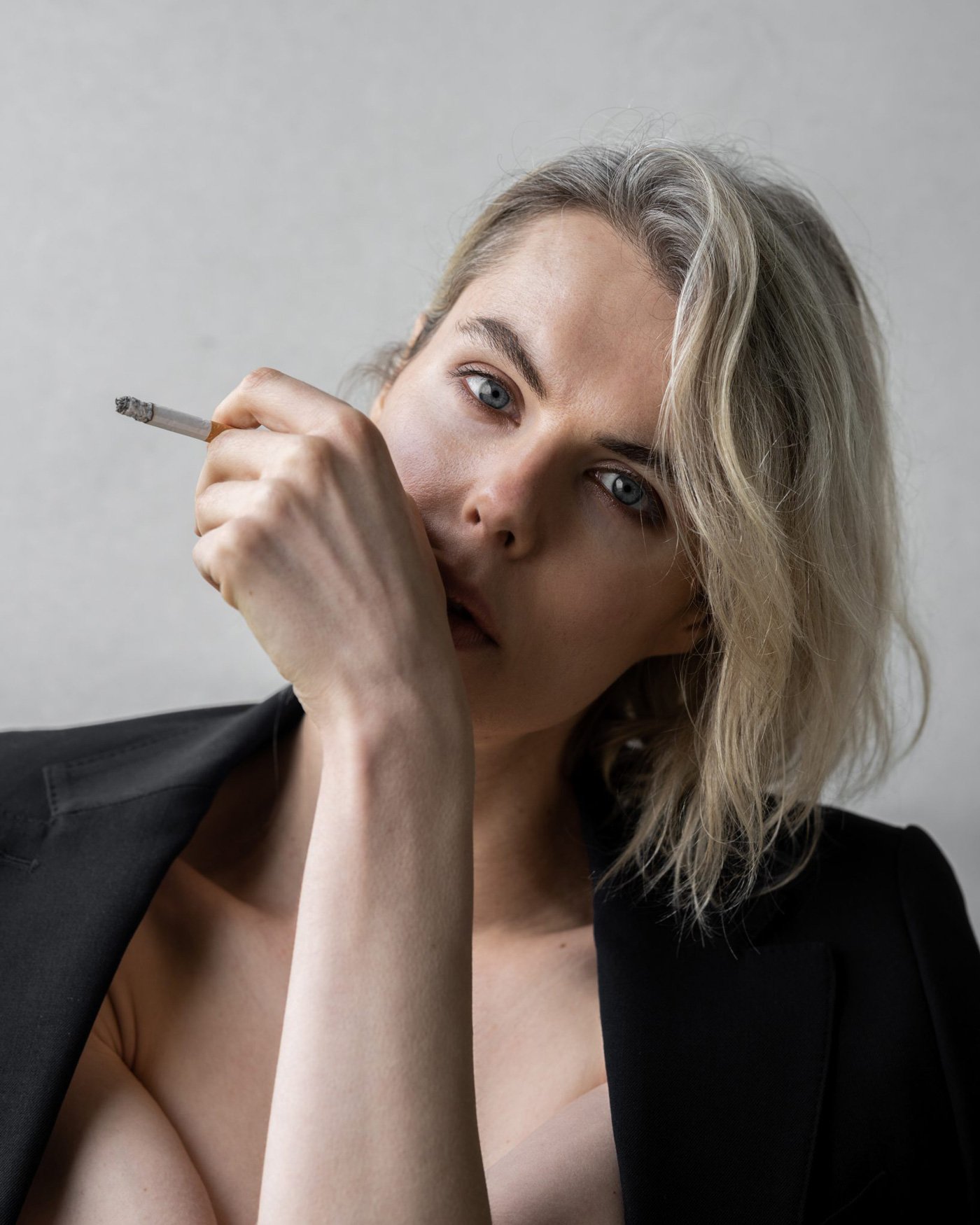 Elsa Léger with blonde, wavy hair and blue eyes holding a lit cigarette near her mouth.