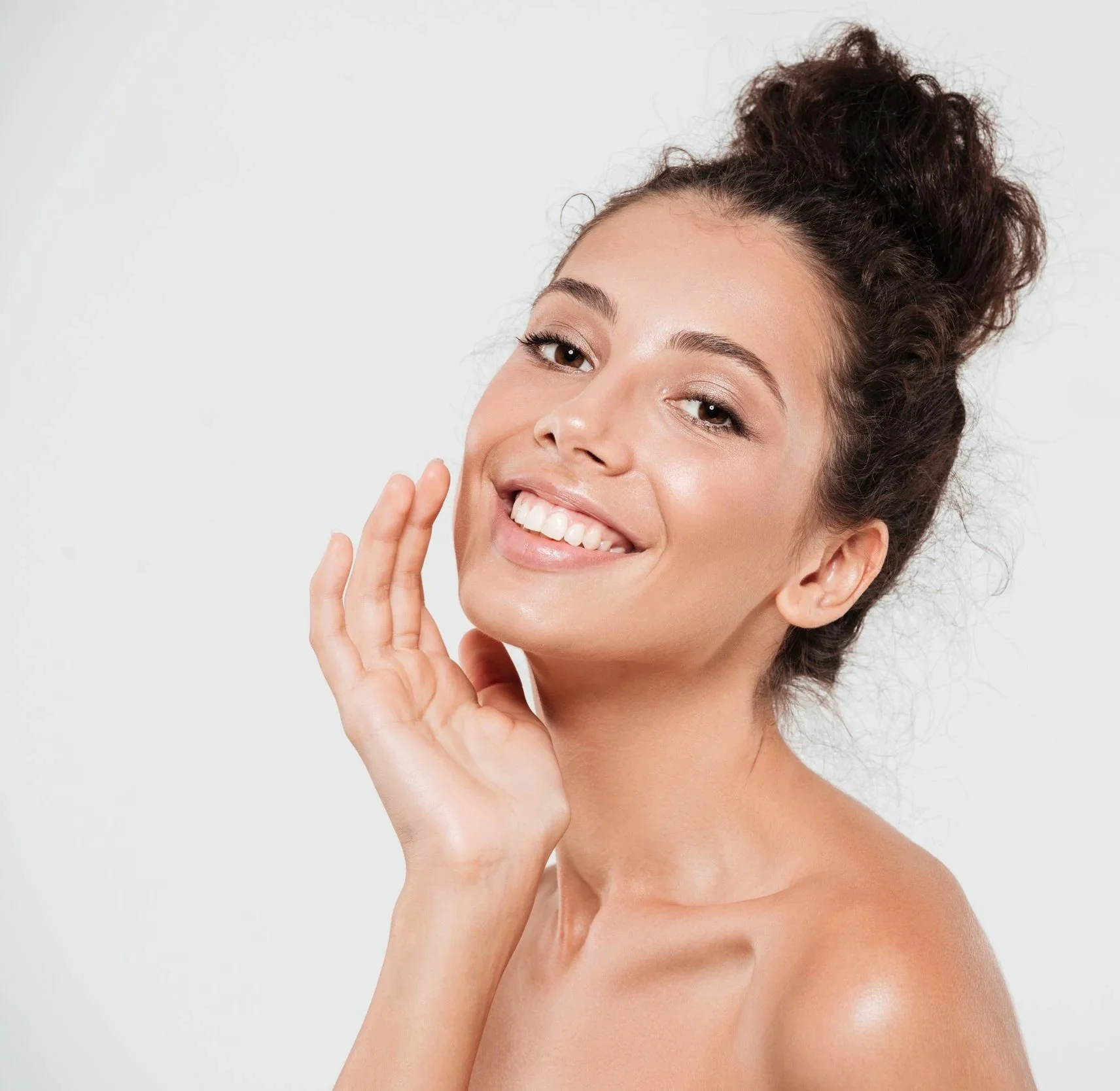 Smiling woman with curly hair touching her face, against a plain white background.