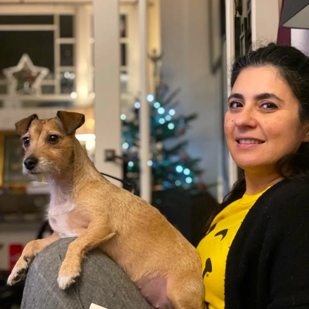 Anoosh Omidi with a small tan and white dog on her lap in a cozy indoor setting.