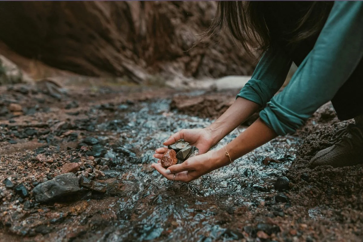 Person collecting small rocks and stones from a stream in a natural outdoor setting.