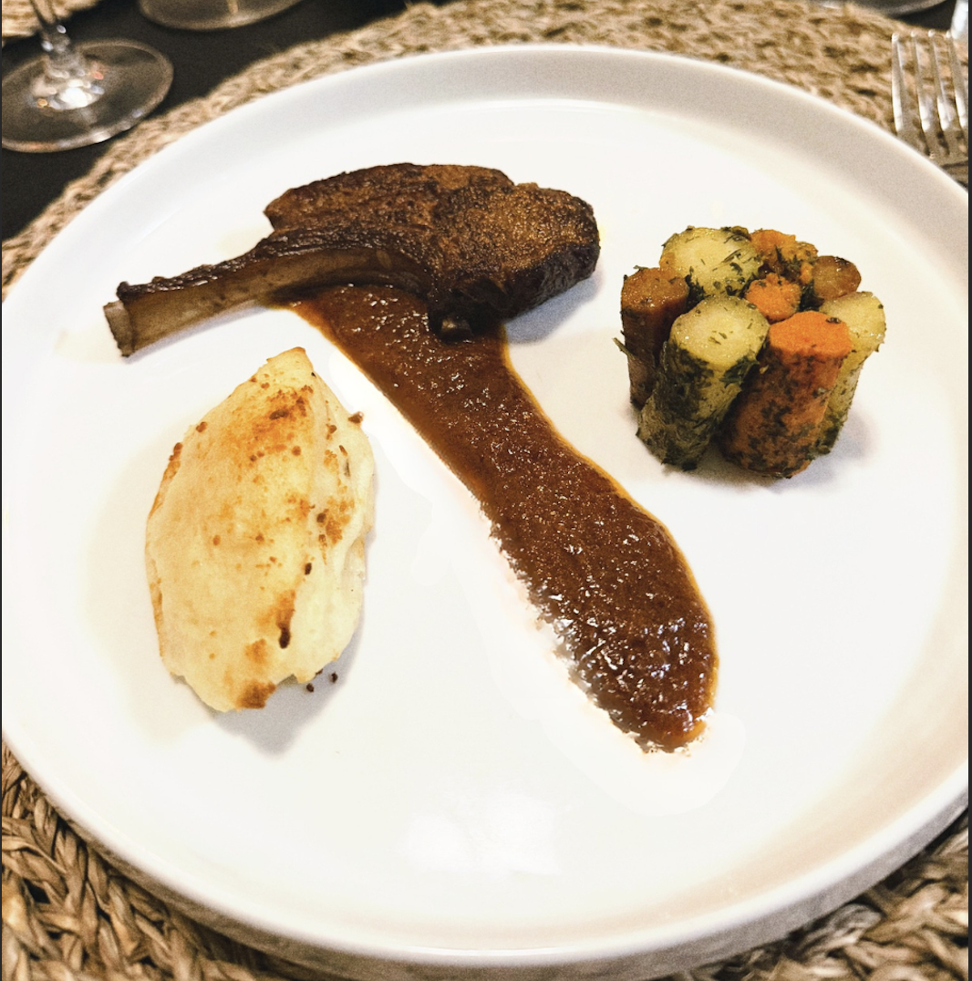 Plate with a roasted lamb chop, a serving of mashed potatoes, and a side of vegetable medley featuring carrots and potatoes with herbs.