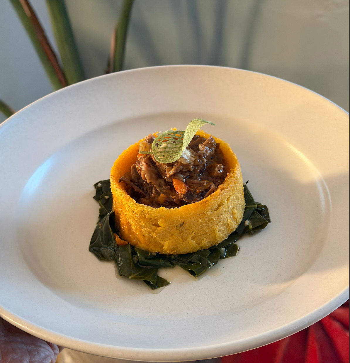 Cornbread muffin filled with beef stew, garnished with a leaf-shaped chip, on a white plate with seaweed underneath.