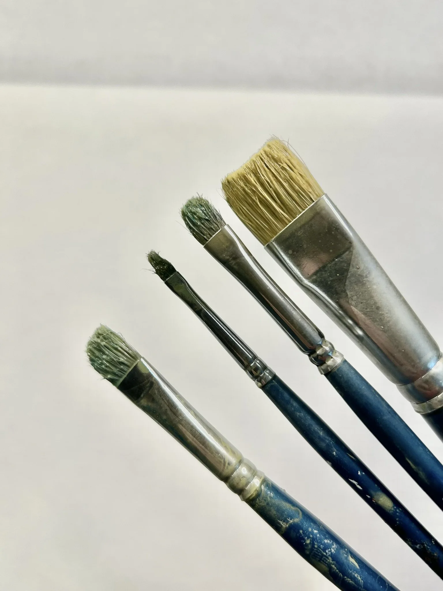 A set of five paintbrushes with varying tip sizes and shapes, painted with different colors, lying against a white background.