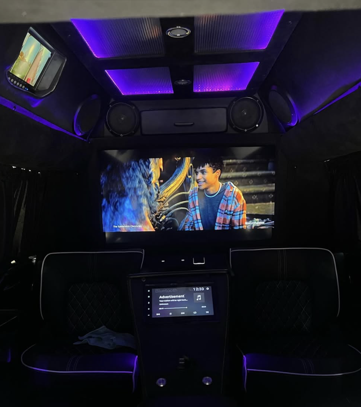 Inside of a custom built 2024 Cadillac Escalade with a 40" tv built into a recessed wall in the rear, purple ambient lighting, and a full custom multimedia system