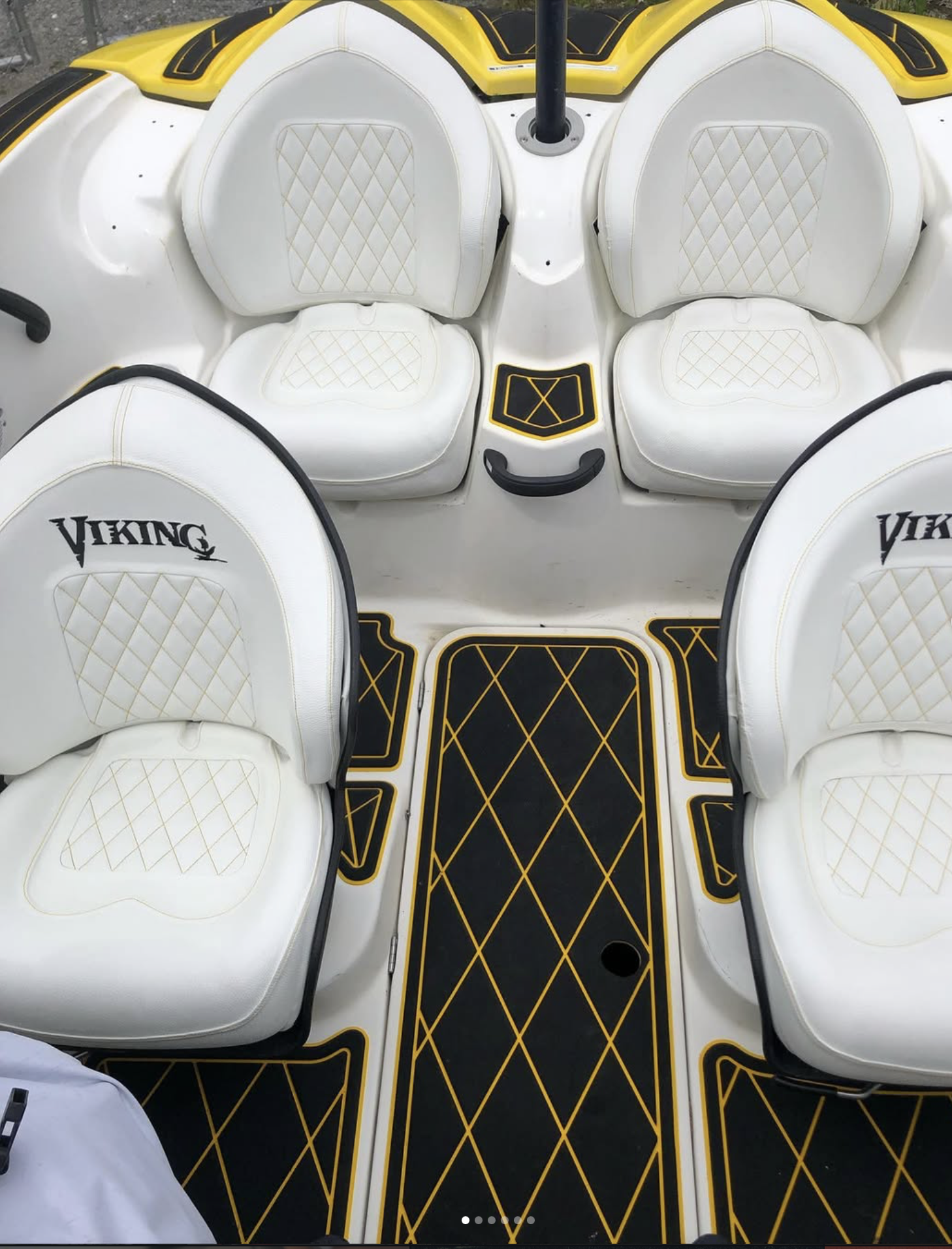The interior of a white and black boat with gold accents, featuring white cushioned seats with diamond quilting and the word 'Viking' embroidered on two of the seats.