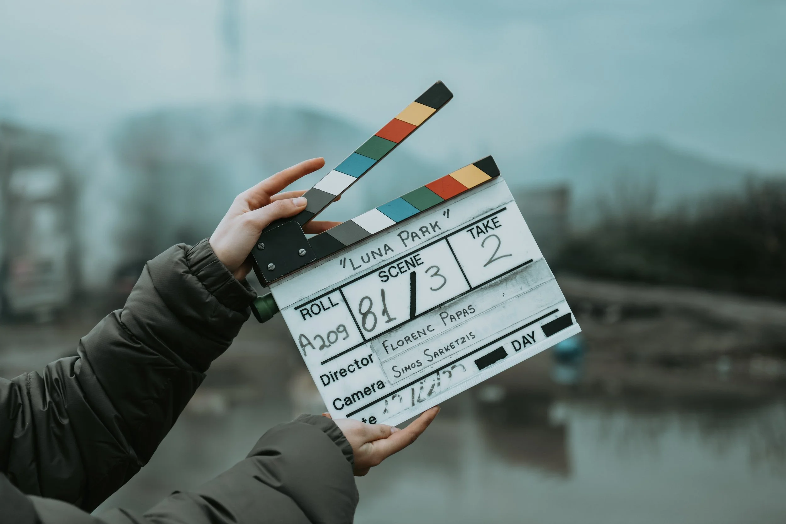 A person holding a film slate board with color calibration strips, set against a blurry outdoor background.